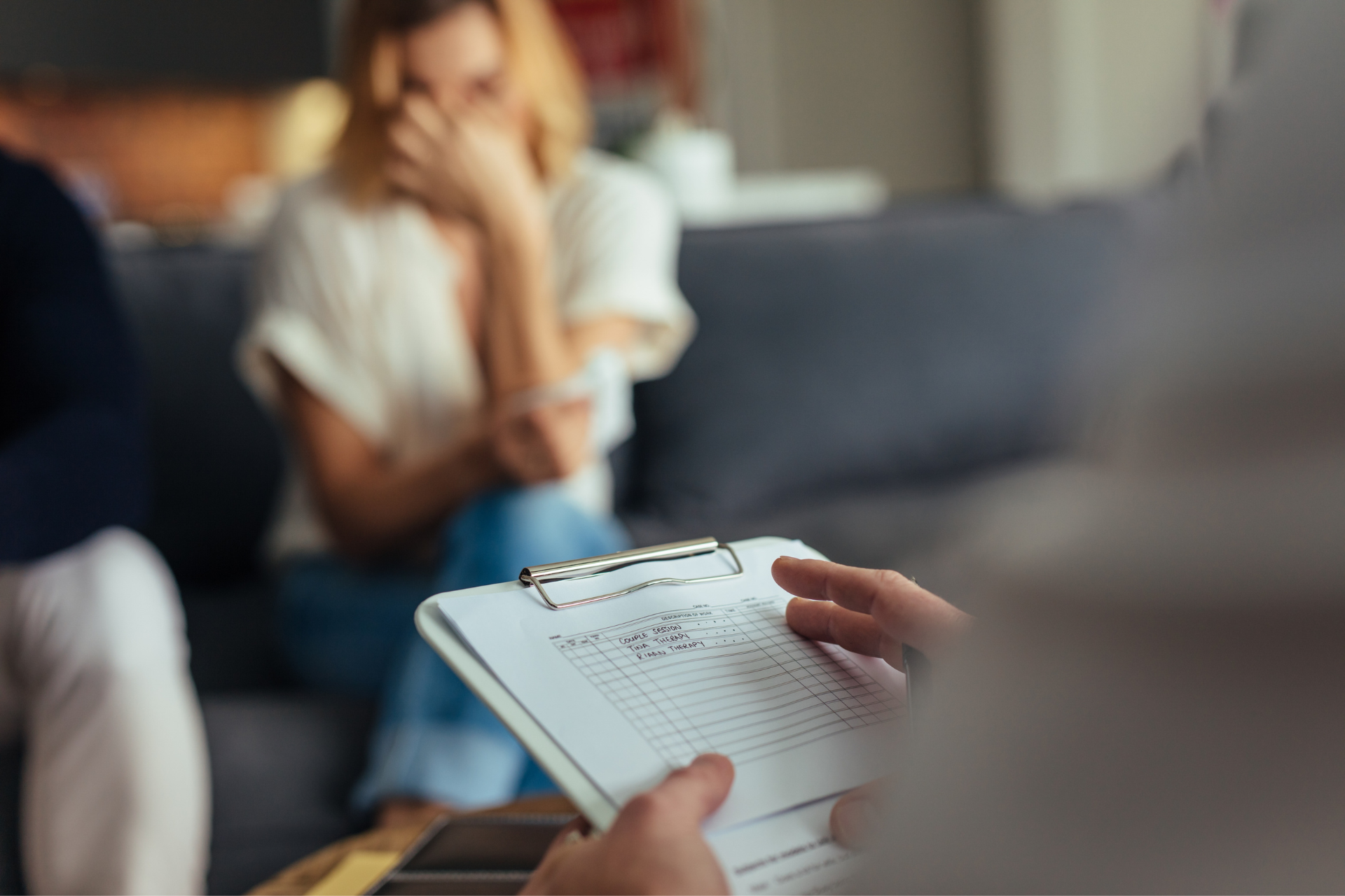 A man is holding a clipboard in front of a woman sitting on a couch.