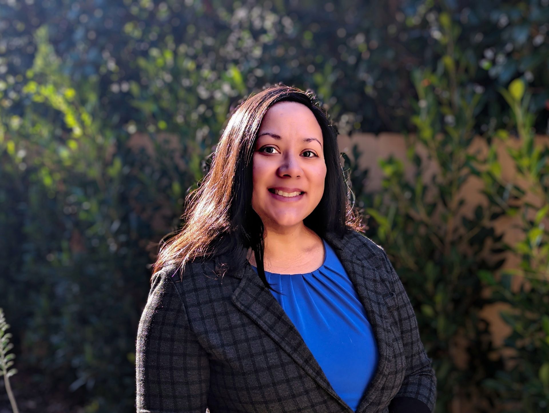 A woman in a blue shirt and gray jacket is smiling for the camera.