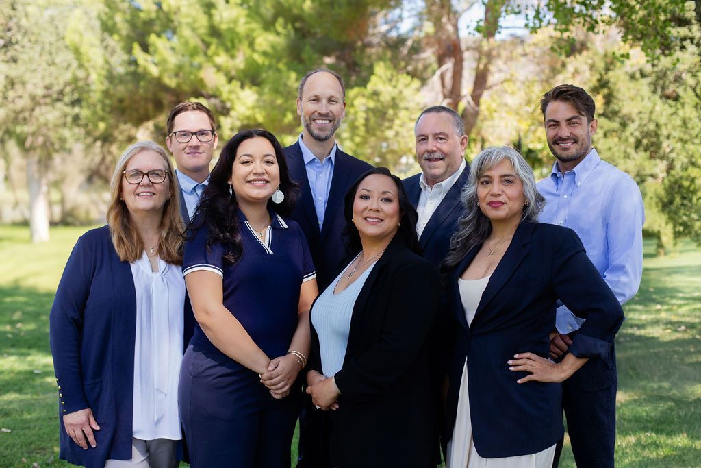 Group of professionals smiling outdoors in a park setting, wearing business attire.