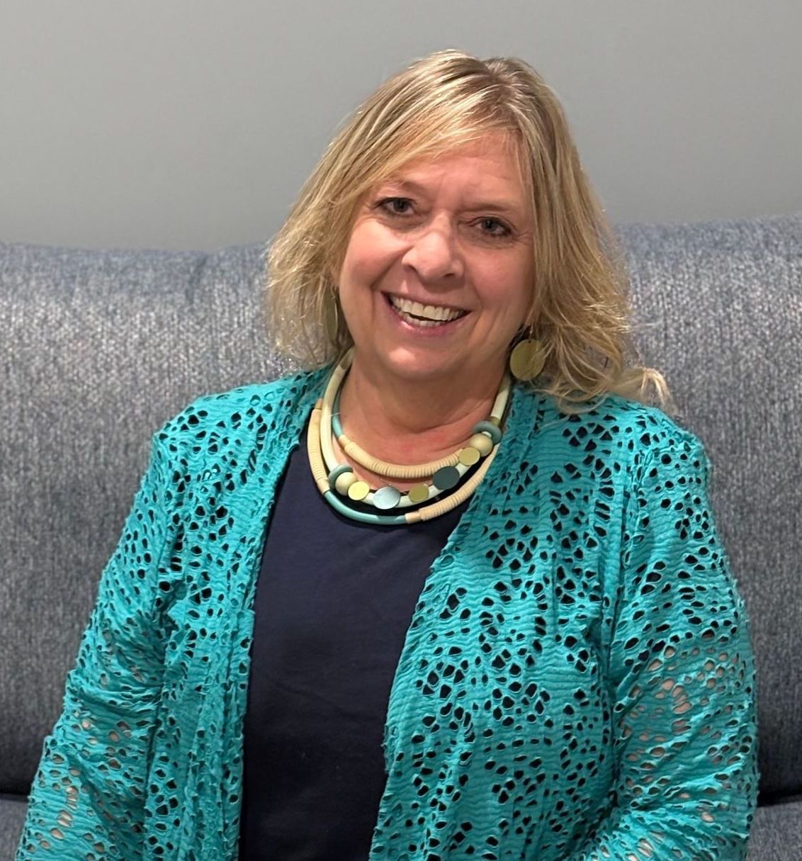 A woman in a blue polka dot shirt is smiling for the camera