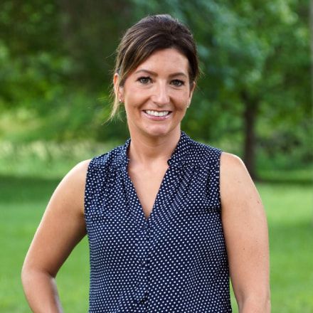 A woman in a blue polka dot shirt is smiling for the camera