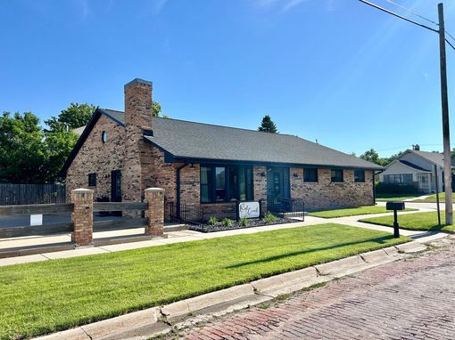 A brick house with a chimney on the roof is sitting on a lush green lawn.