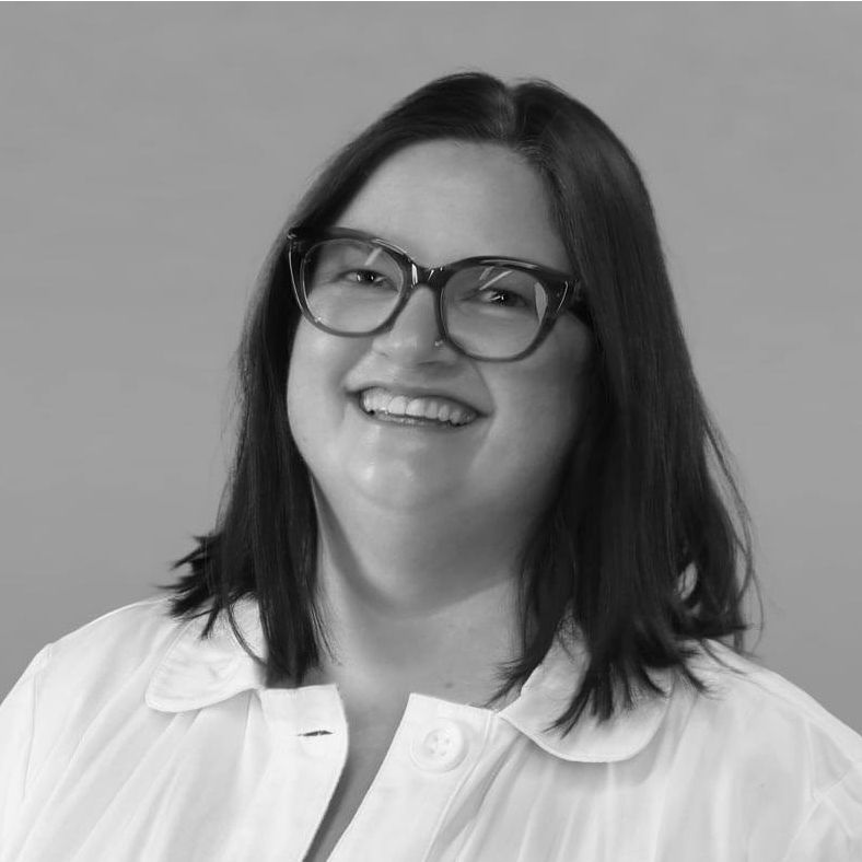 A woman wearing glasses and a white shirt is smiling in a black and white photo.