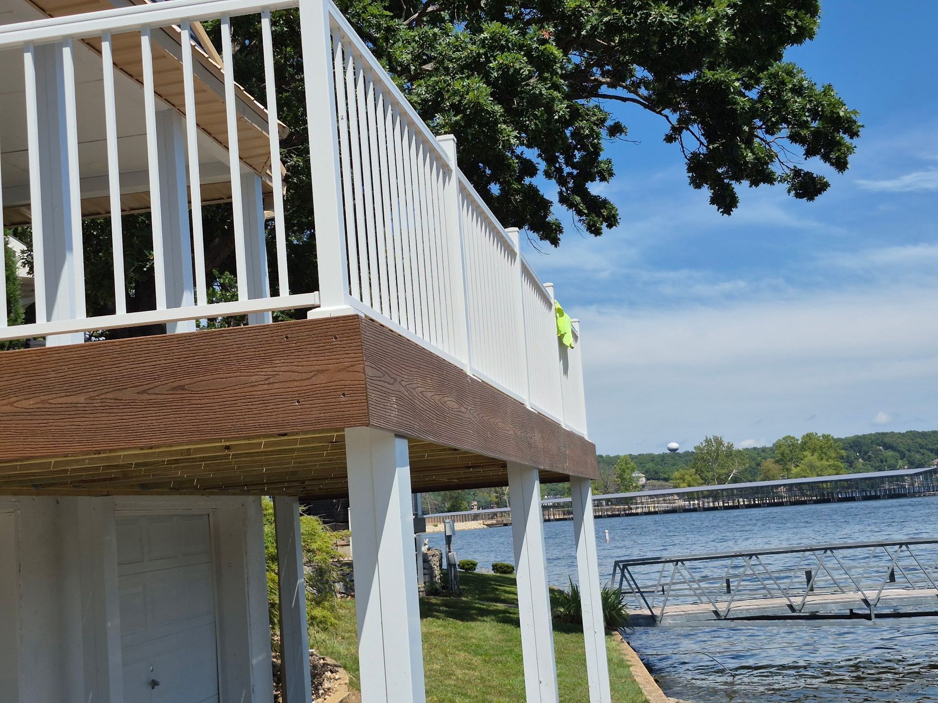A low-angle view of a white deck with wood-grain trim overlooking a lake, with a dock visible in the water.