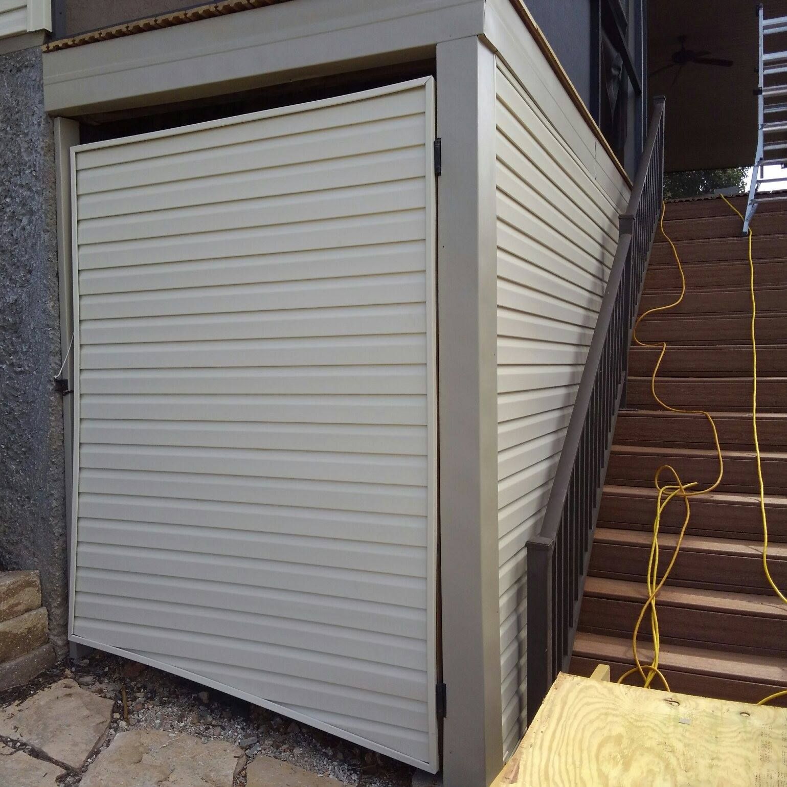 Tan siding covers an enclosure next to wooden stairs; a door is ajar.