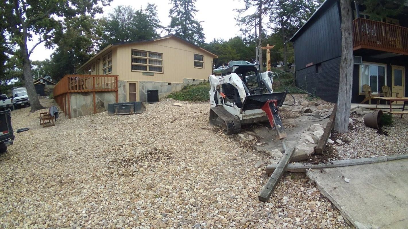 Bobcat excavator on a gravel-covered construction site in front of a house, breaking up concrete.