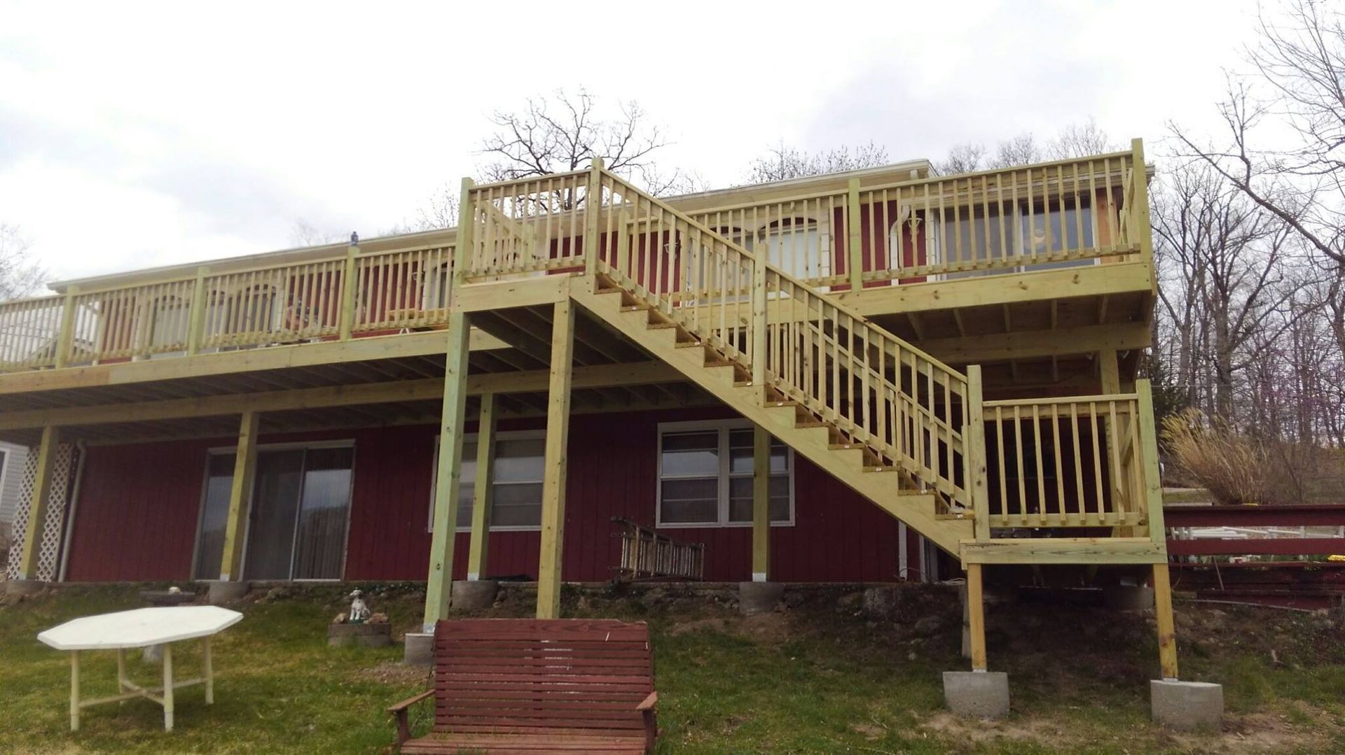 Wooden deck with stairs attached to a red house, surrounded by grass and trees.
