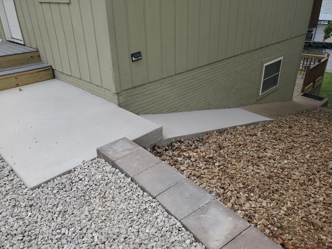 Concrete steps leading to a building with tan siding, next to gravel and a retaining wall.