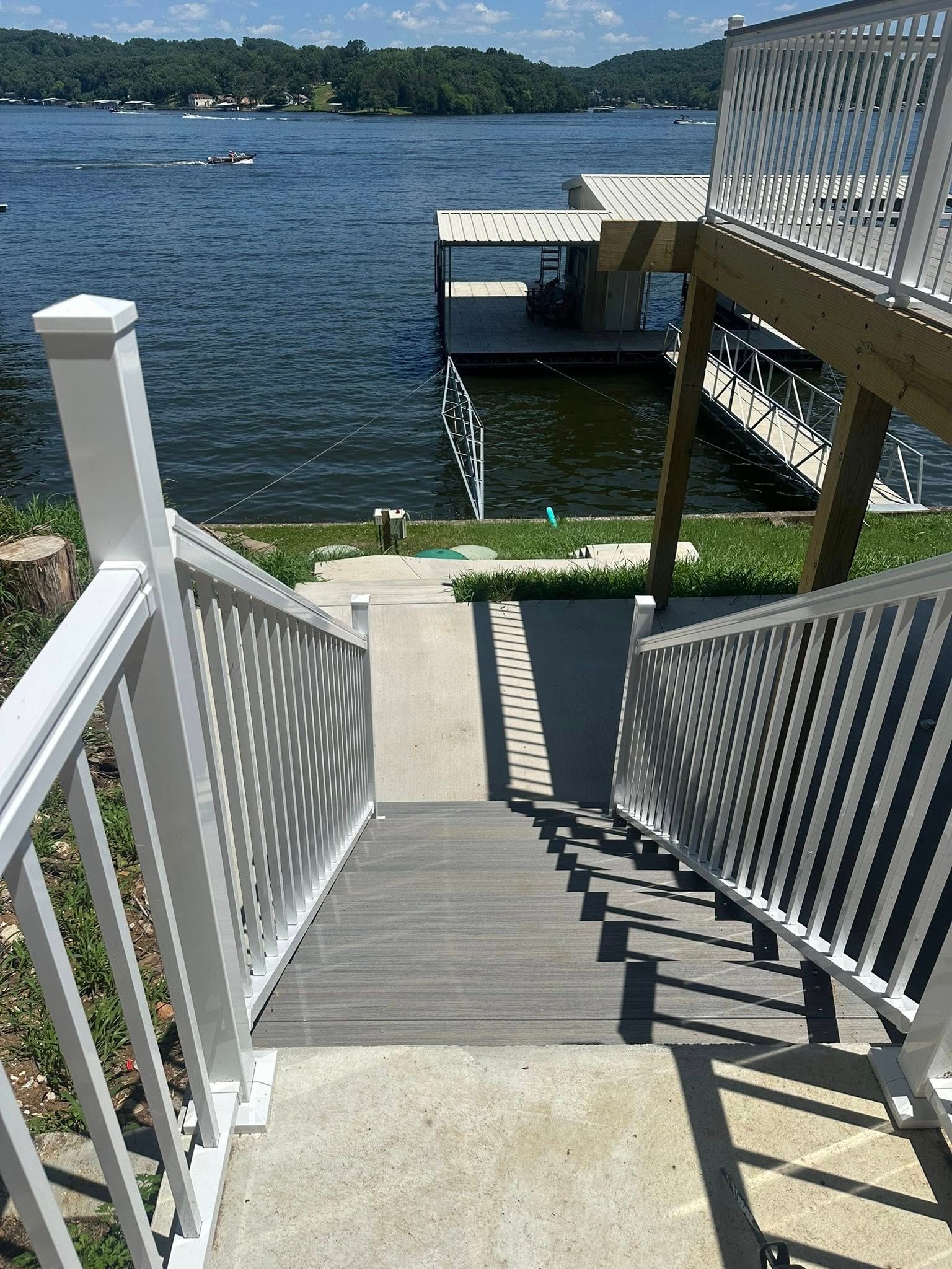 Stairs leading down to a lakefront dock with white railing on a sunny day.