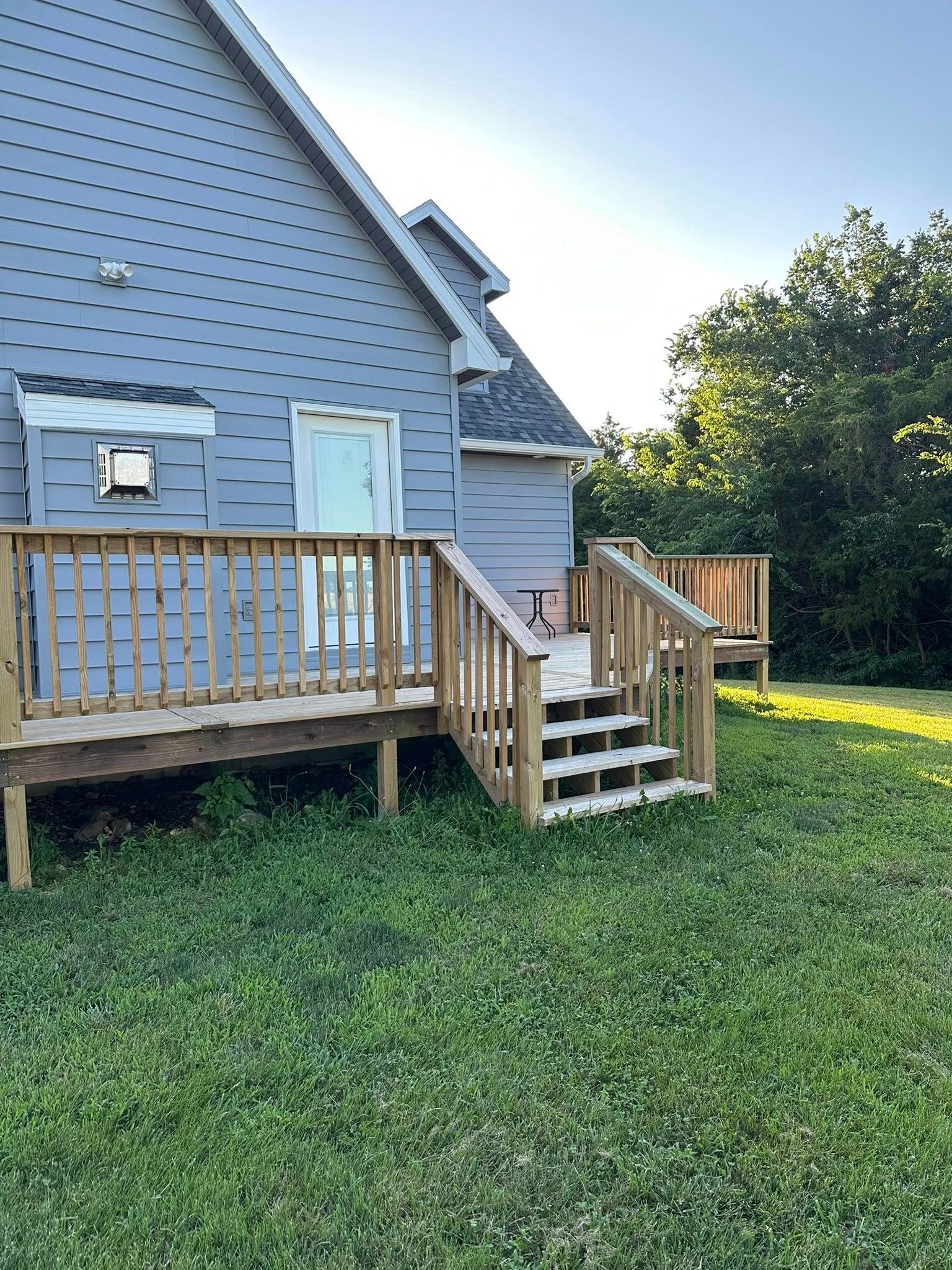 Wooden deck attached to a gray house, with stairs leading down to a grassy yard.
