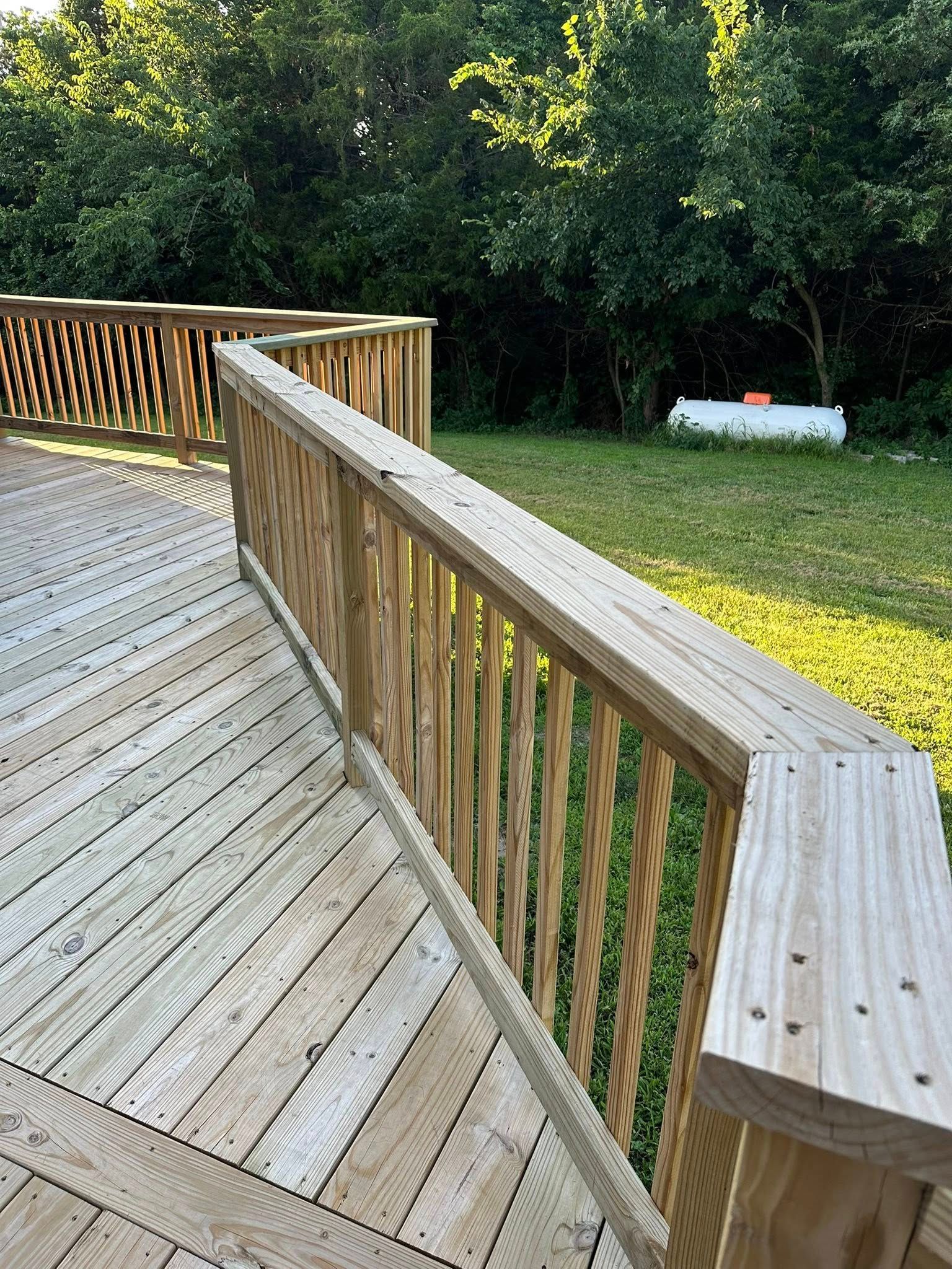 Wooden deck with railing, a propane tank in the background, and trees.