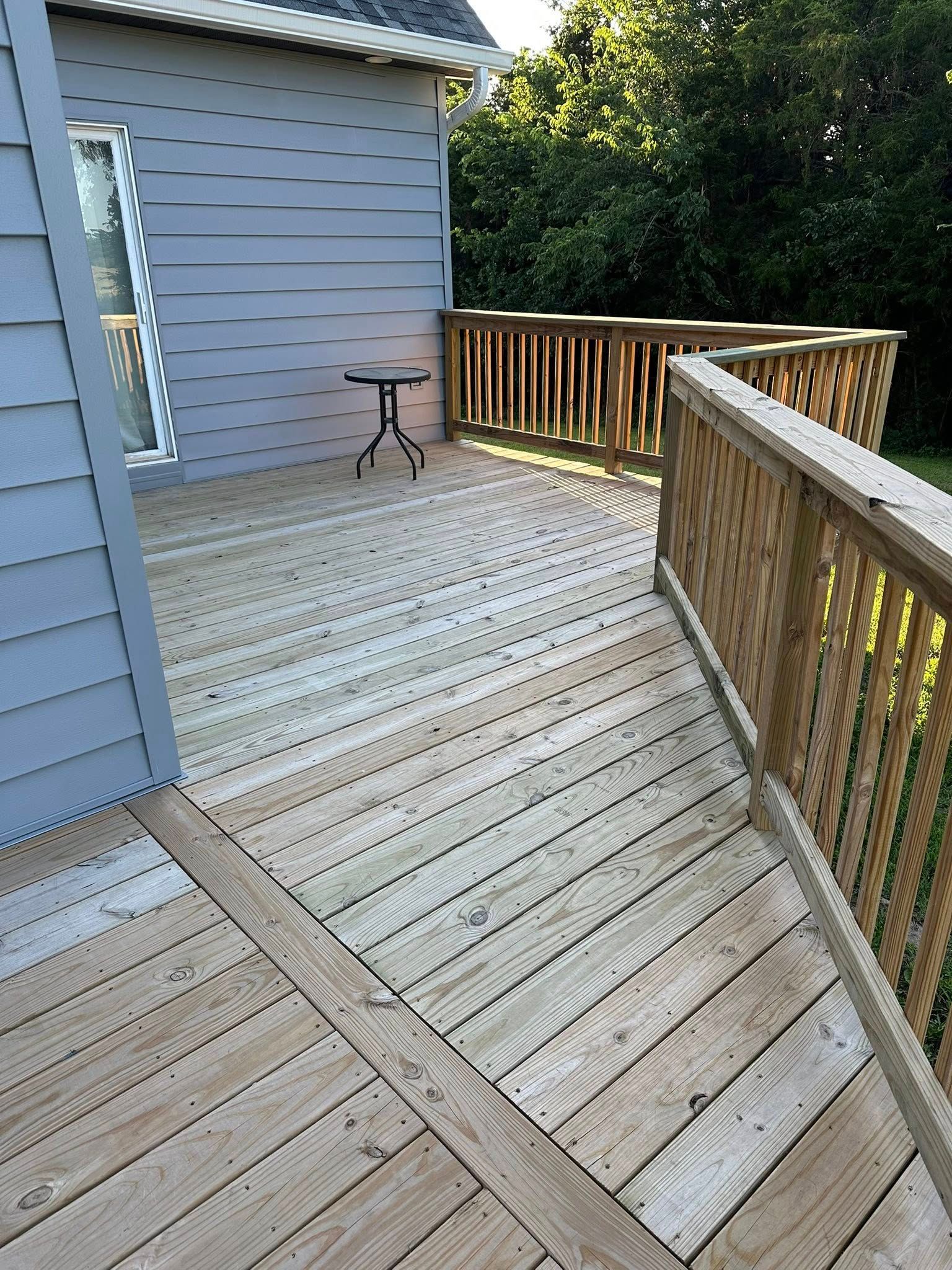 Wooden deck with railings, next to a blue house. A small black table sits on the deck.