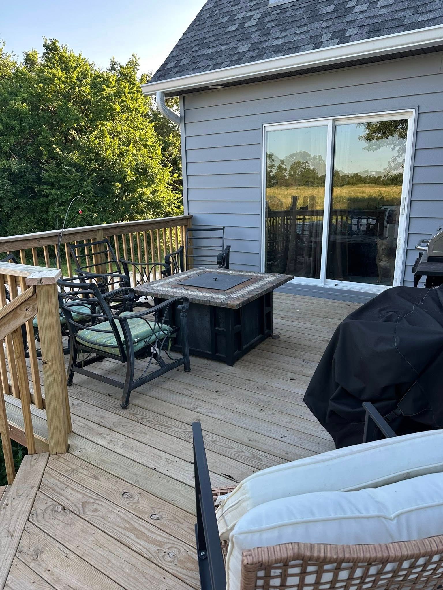 Wooden deck with patio furniture, fire pit, and grill, next to a house with sliding glass doors.