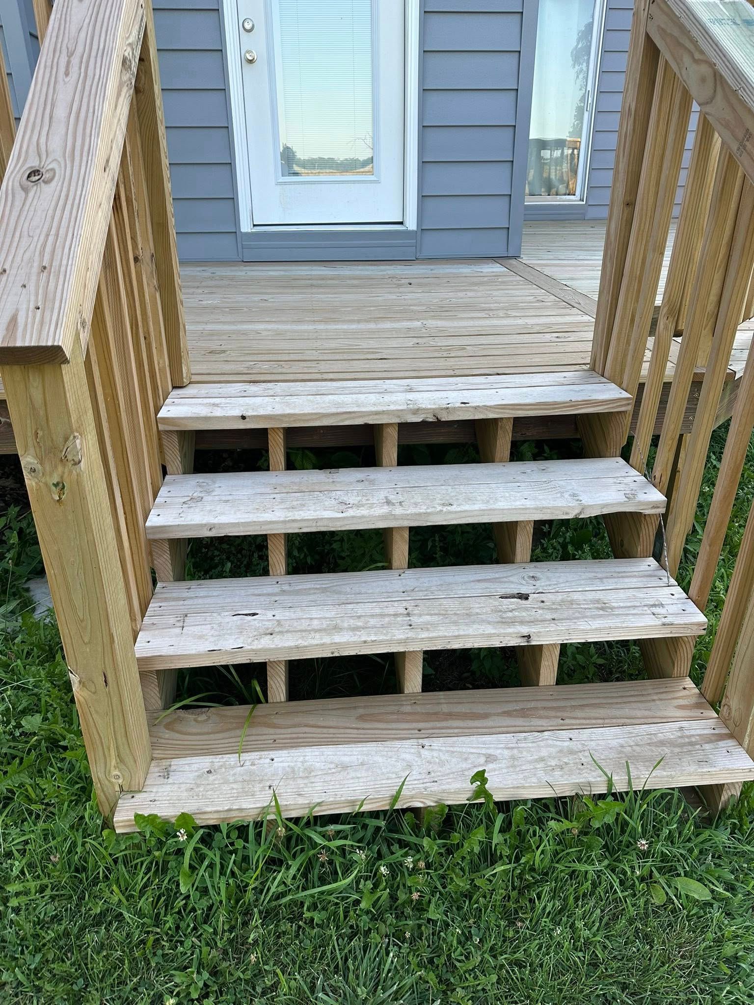 Wooden outdoor steps leading to a door, with weathered wood and grassy surroundings.