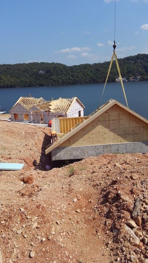 Construction of houses near a lake, crane lifting roof section.