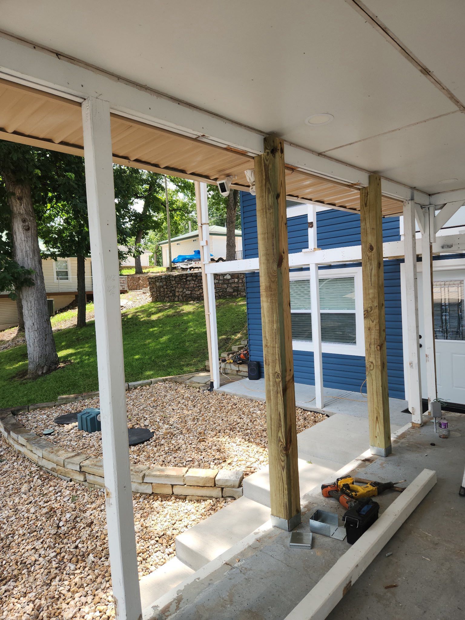 A porch under construction with wooden and white support columns, gravel, and blue house in the background.