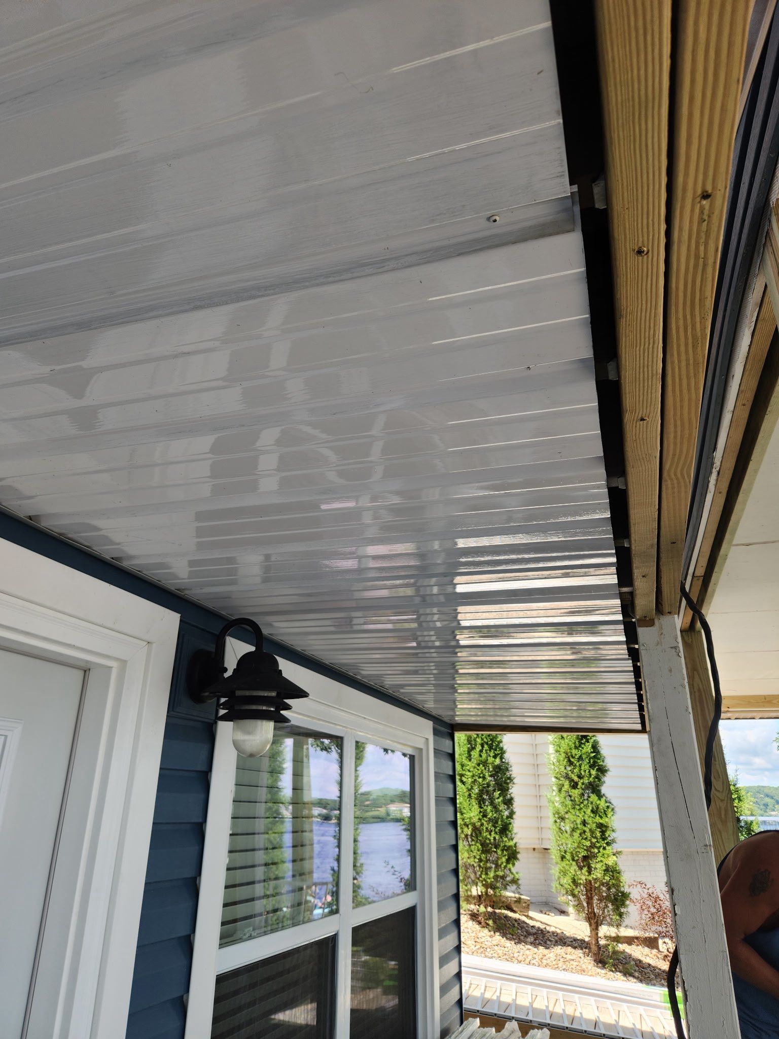 White and silver ceiling panels installed under an eave, with a blue house and window visible.
