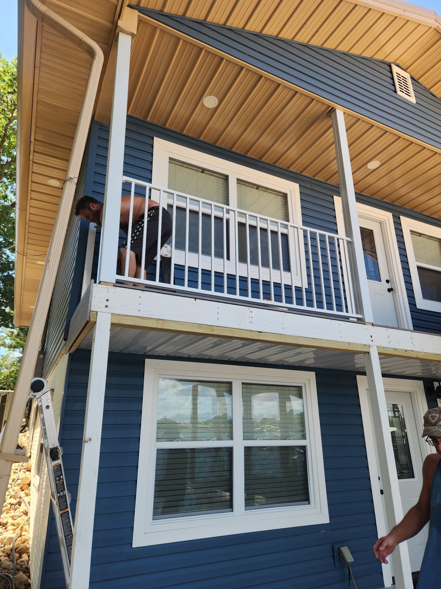 Blue house with white trim, a person on a second-story balcony, and a ladder.