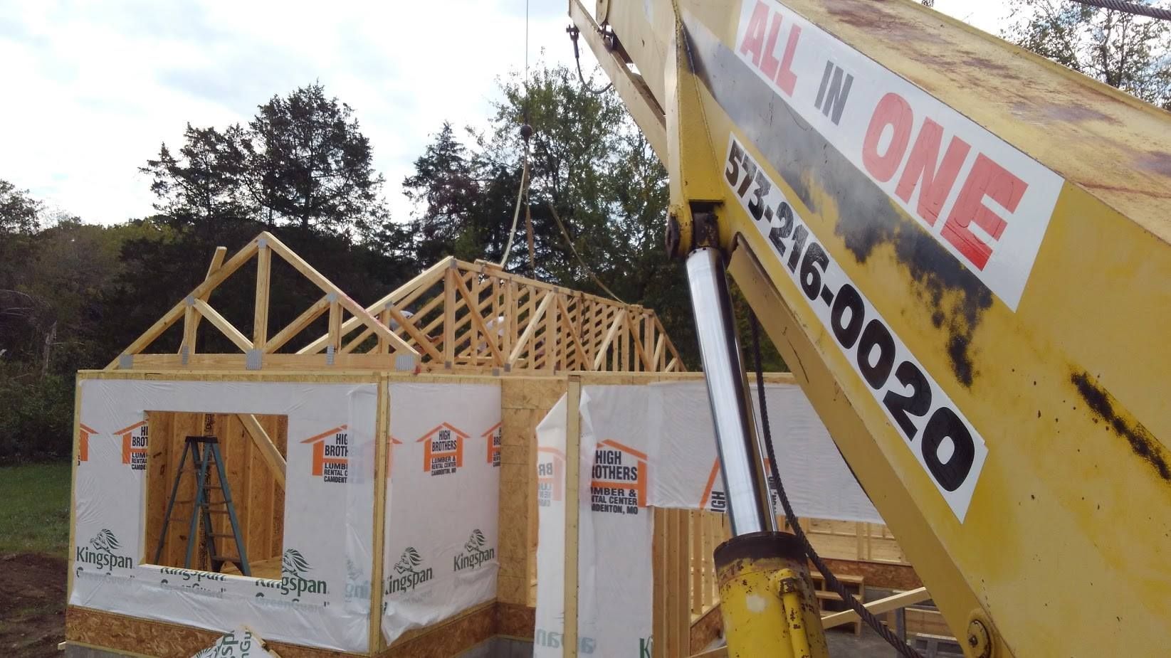 A crane placing wooden roof trusses on a house under construction.