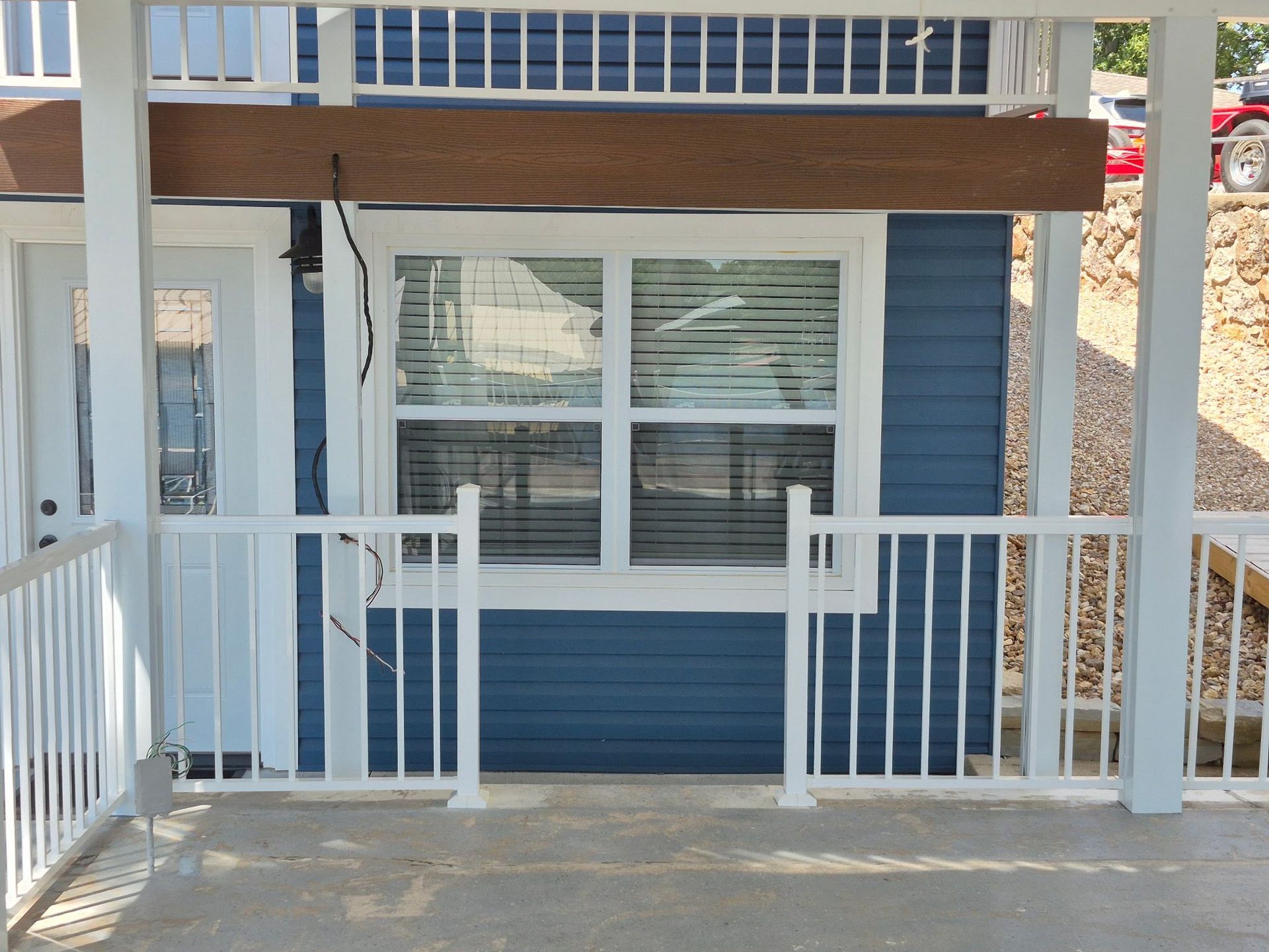 Blue building exterior with white railing and trim, window with blinds, and brown beam.