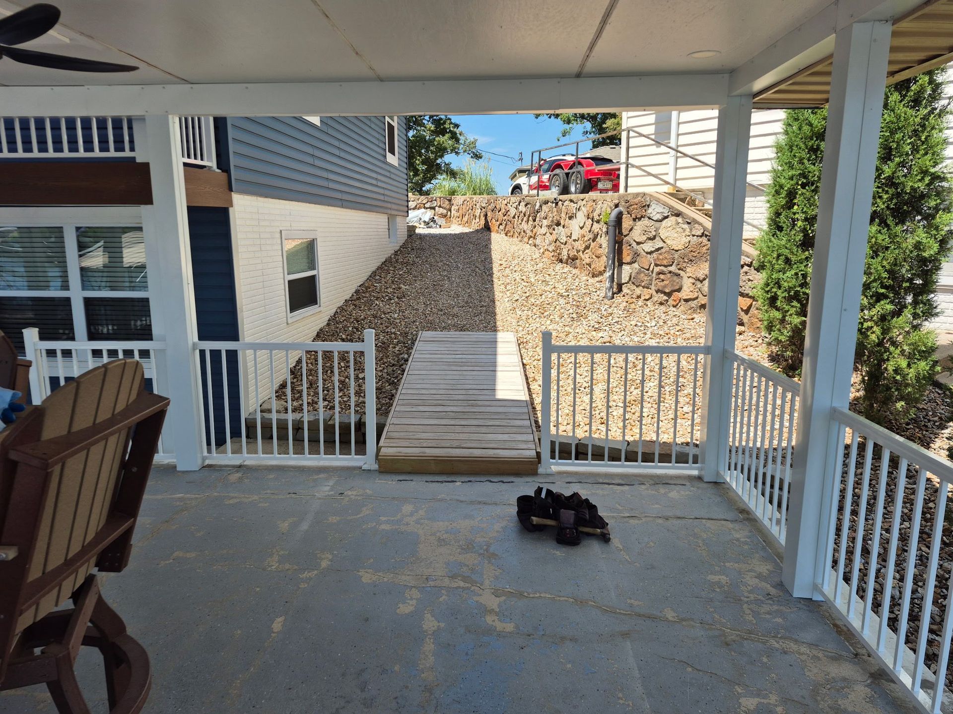 A porch overlooks a wooden walkway leading uphill; a blue house and red car are visible.