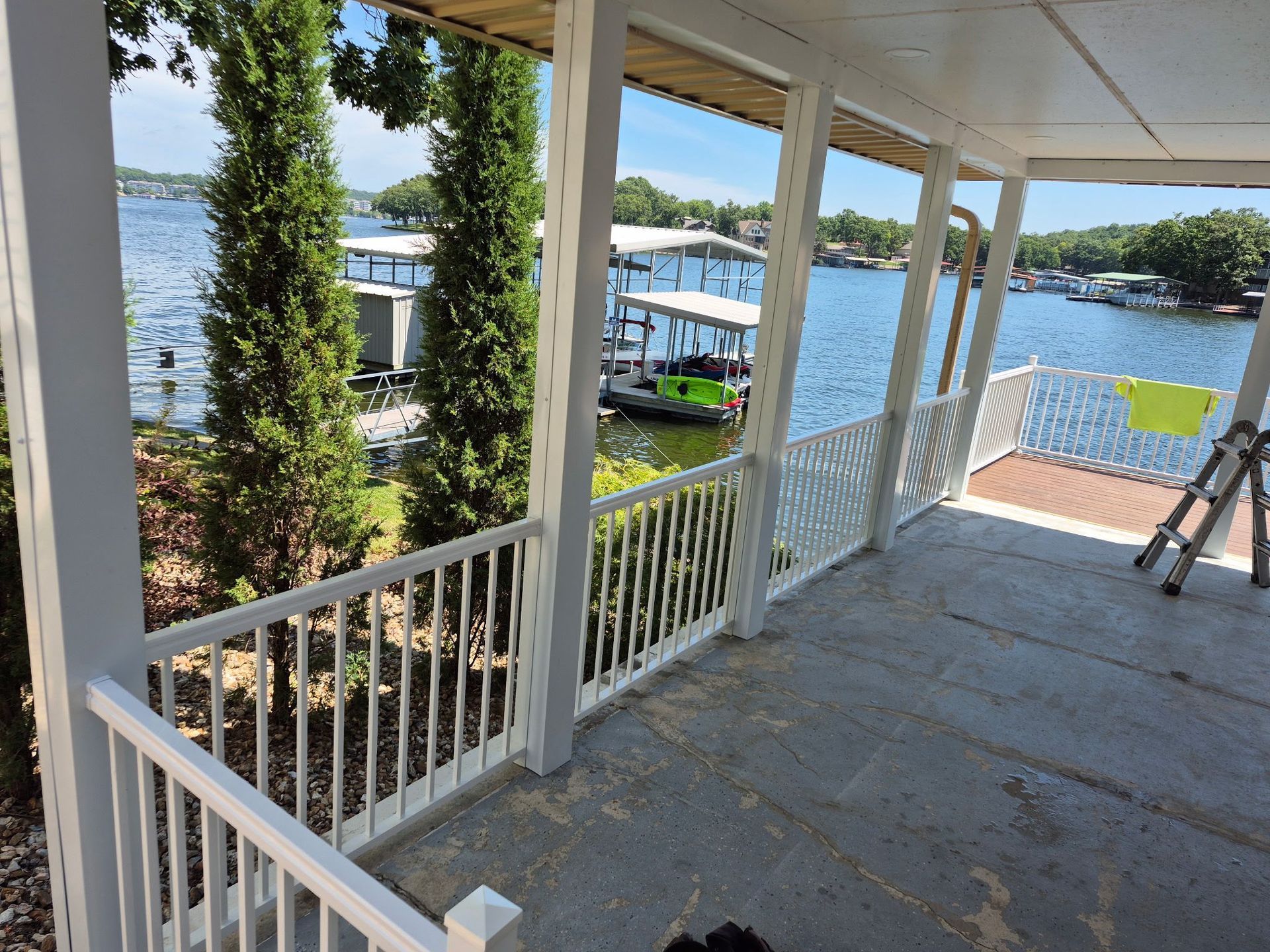 Porch overlooking a lake with white railing and trees. A boat dock is visible in the water.