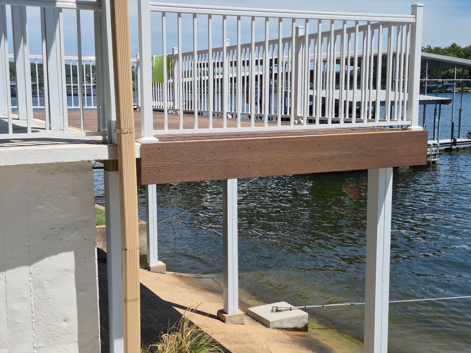 White railing, deck extending over water supported by white posts. Brown wood beams visible.