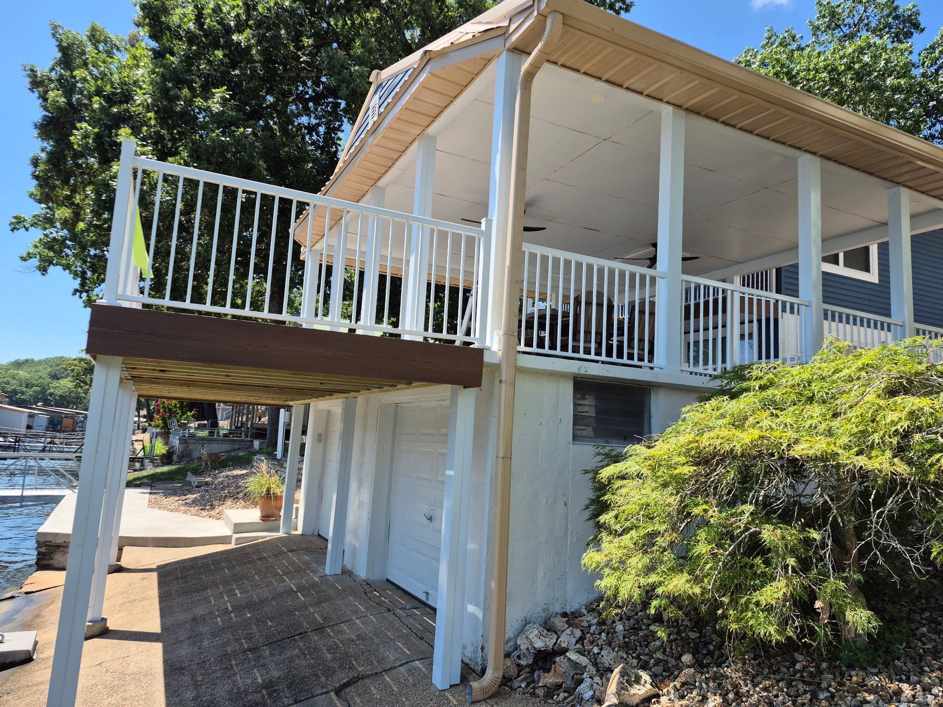 White waterfront home with covered deck, overlooking water; beige siding, white railings.
