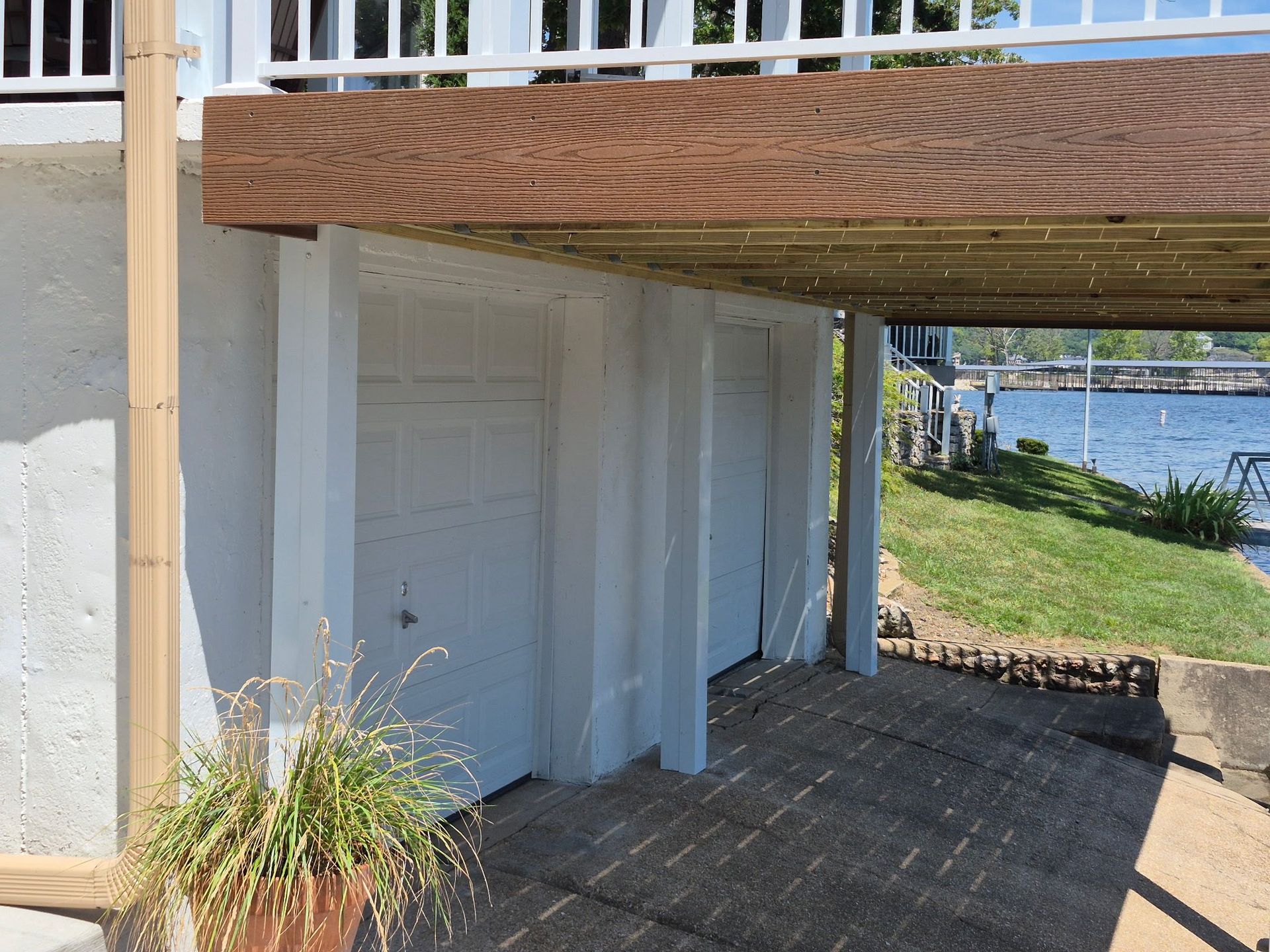 White garage doors under a wooden deck, partially obscured by white curtains, next to a lake.
