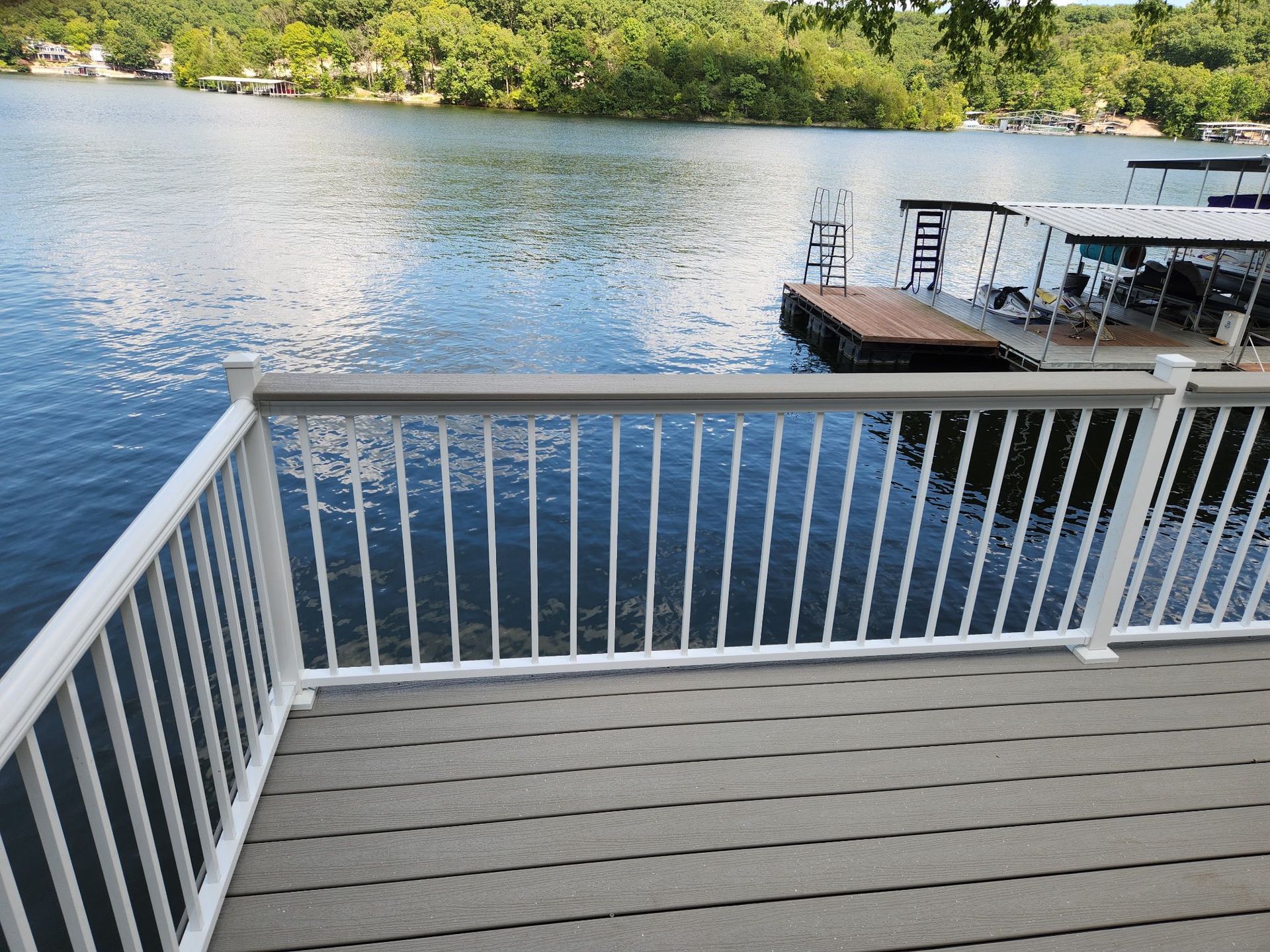 Deck overlooking a lake with a dock; trees and houses in the background.