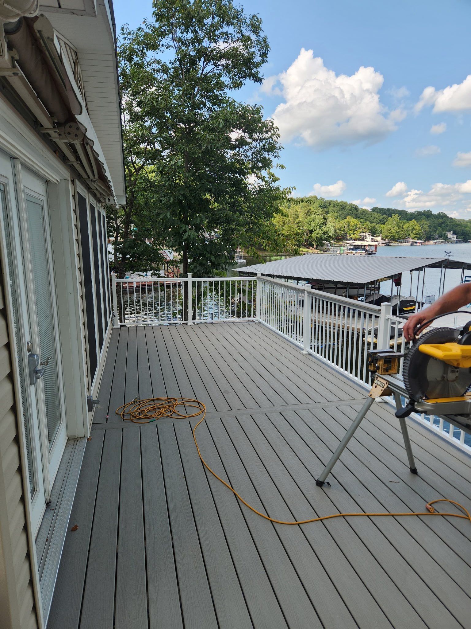 Deck with composite boards, white railing, and water view. A person uses a saw.
