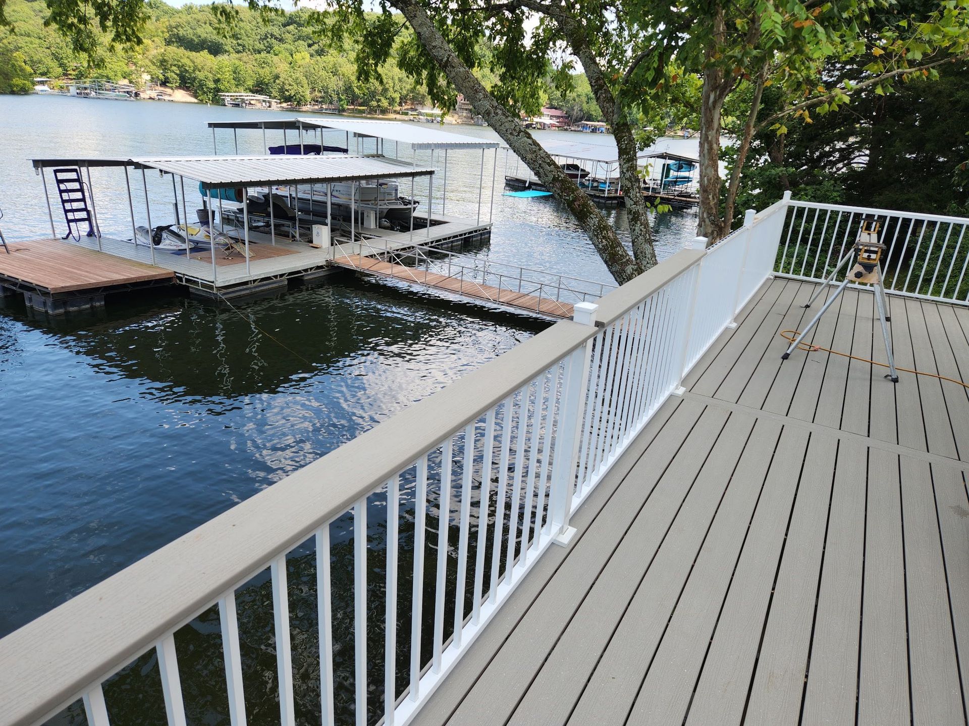 Deck overlooking a lake with docks, trees, and blue water. White railing and composite deck.