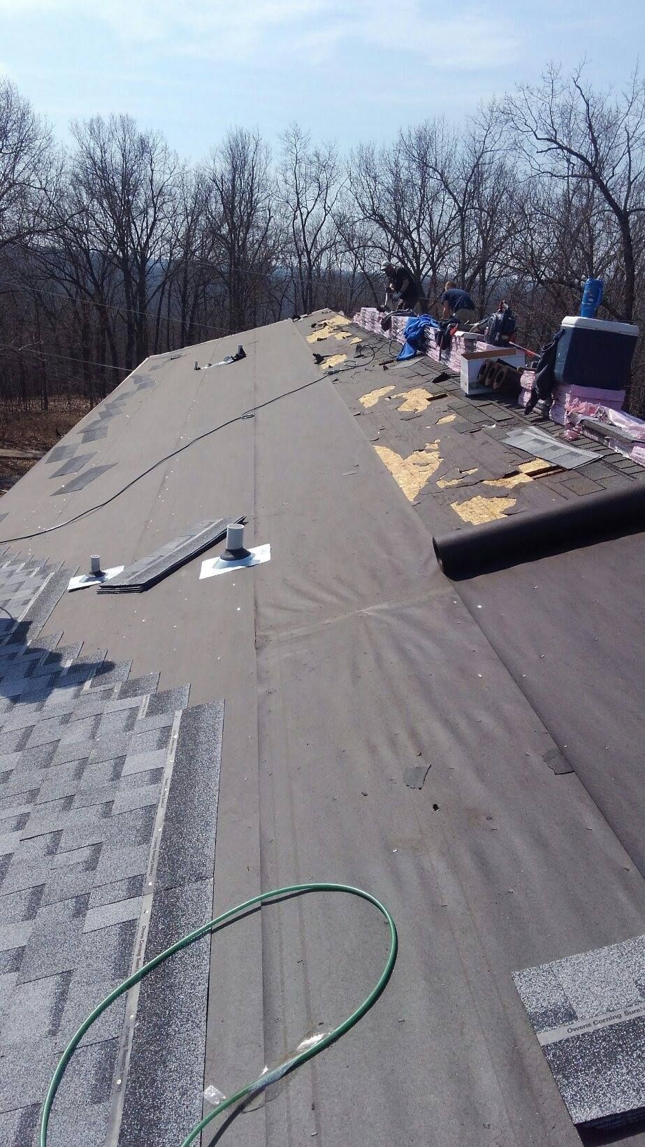 Roof being repaired with asphalt shingles. A green hose and tools are present.