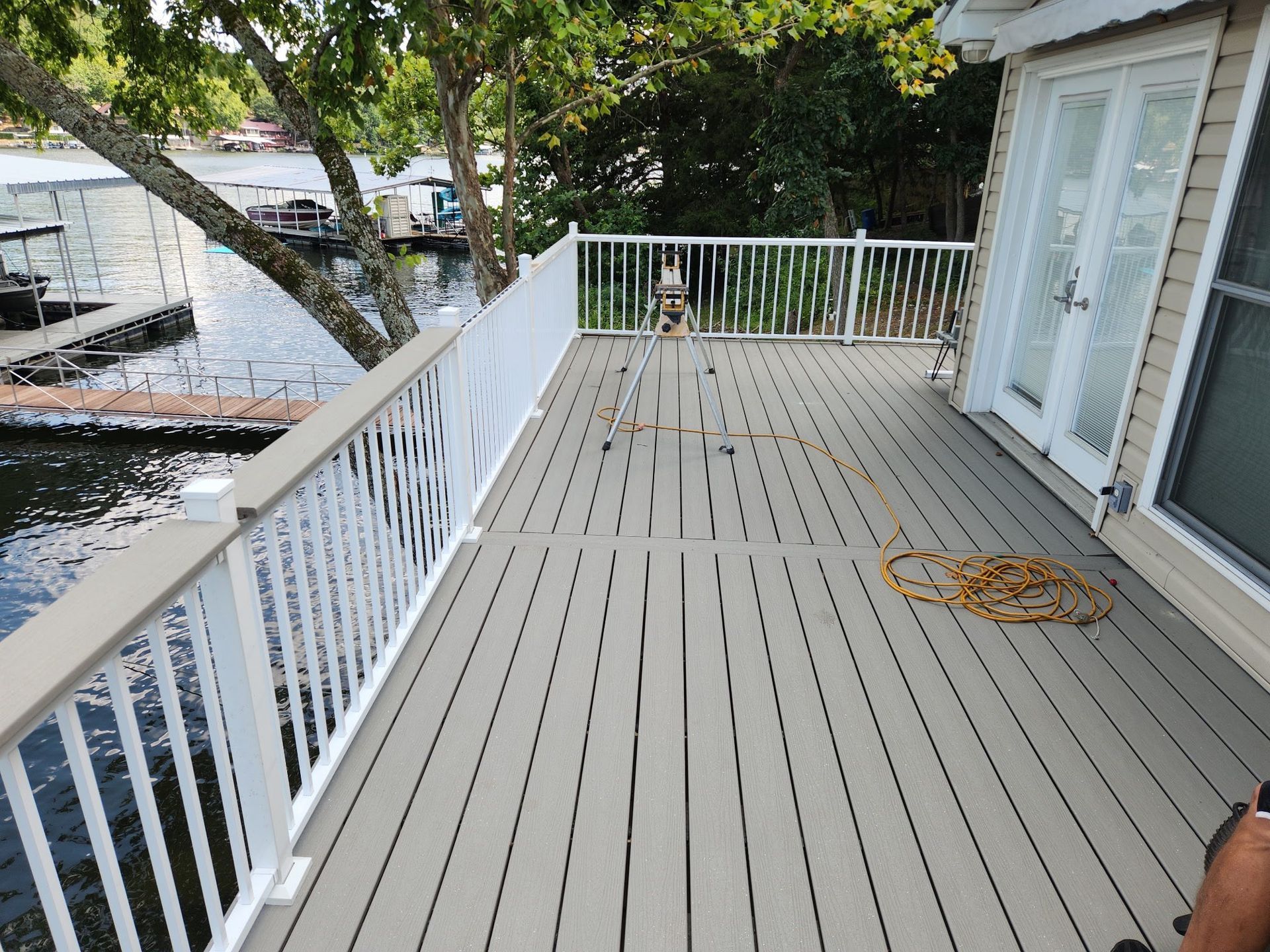 Deck overlooking water with white railing and doors. Yellow extension cord on deck.