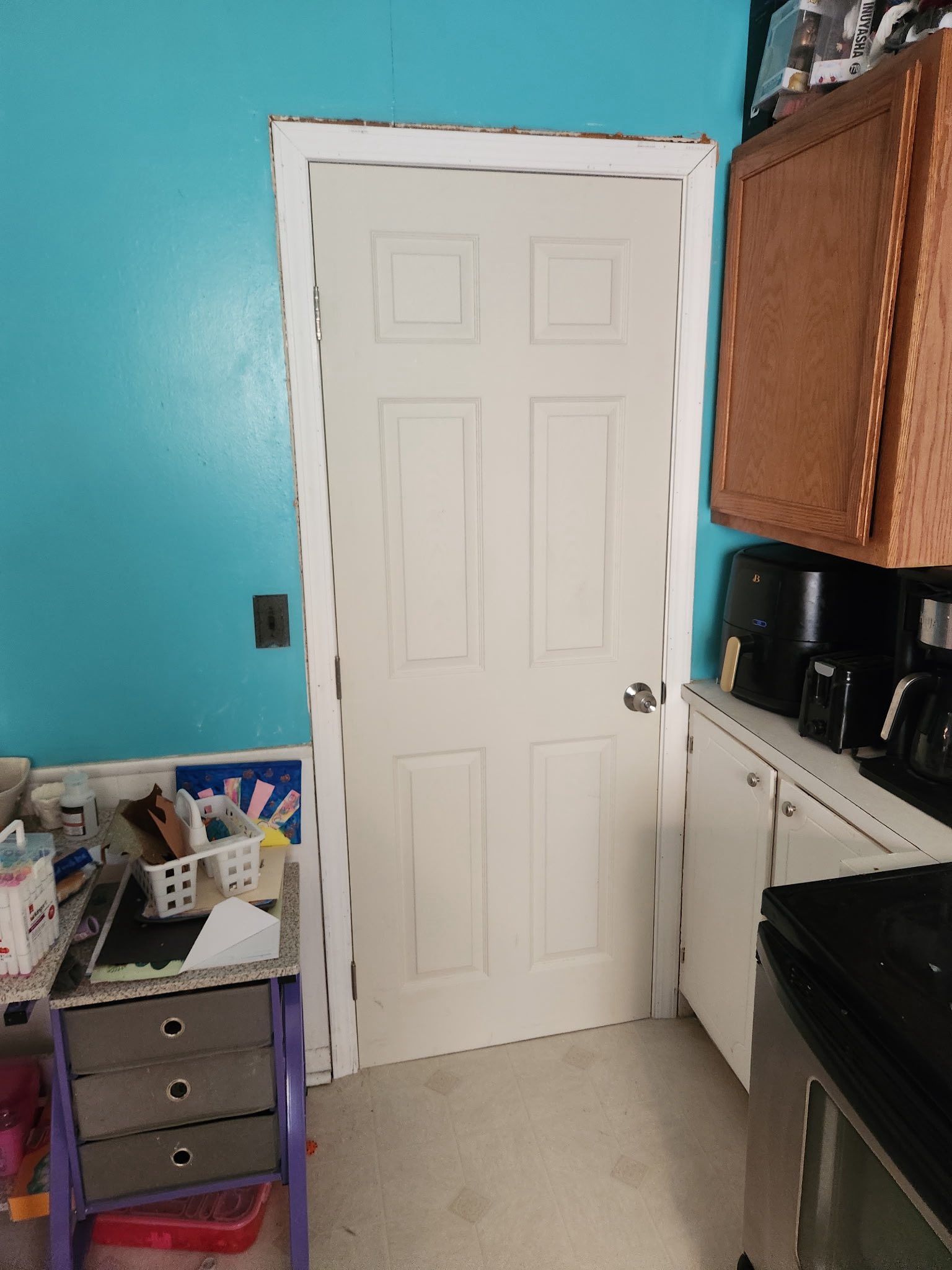 White door in a room with blue wall, cabinets, and appliances.