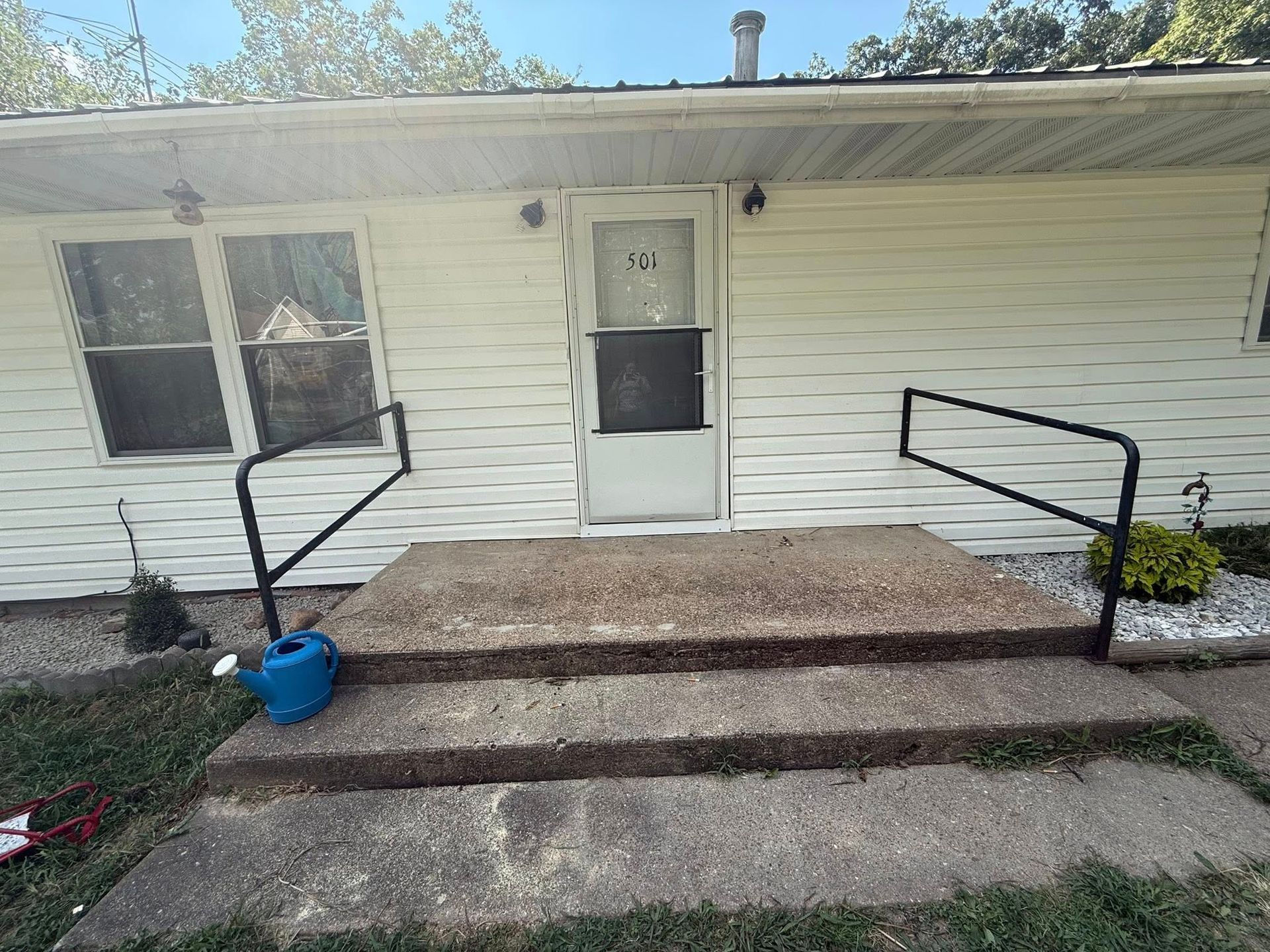 Exterior of a white house with steps leading to a front door. Black handrails are on both sides of the steps.