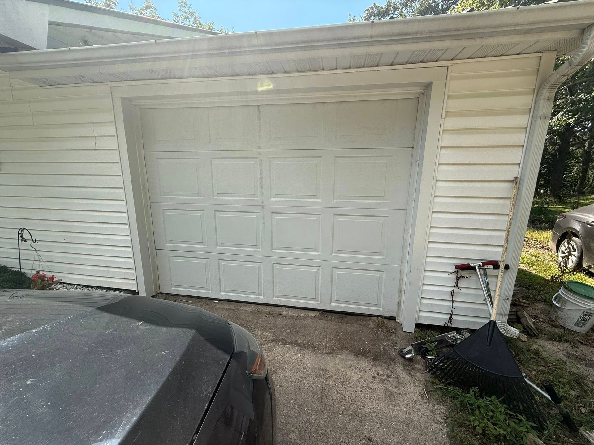White garage door on a white sided building with a car parked partially in front.
