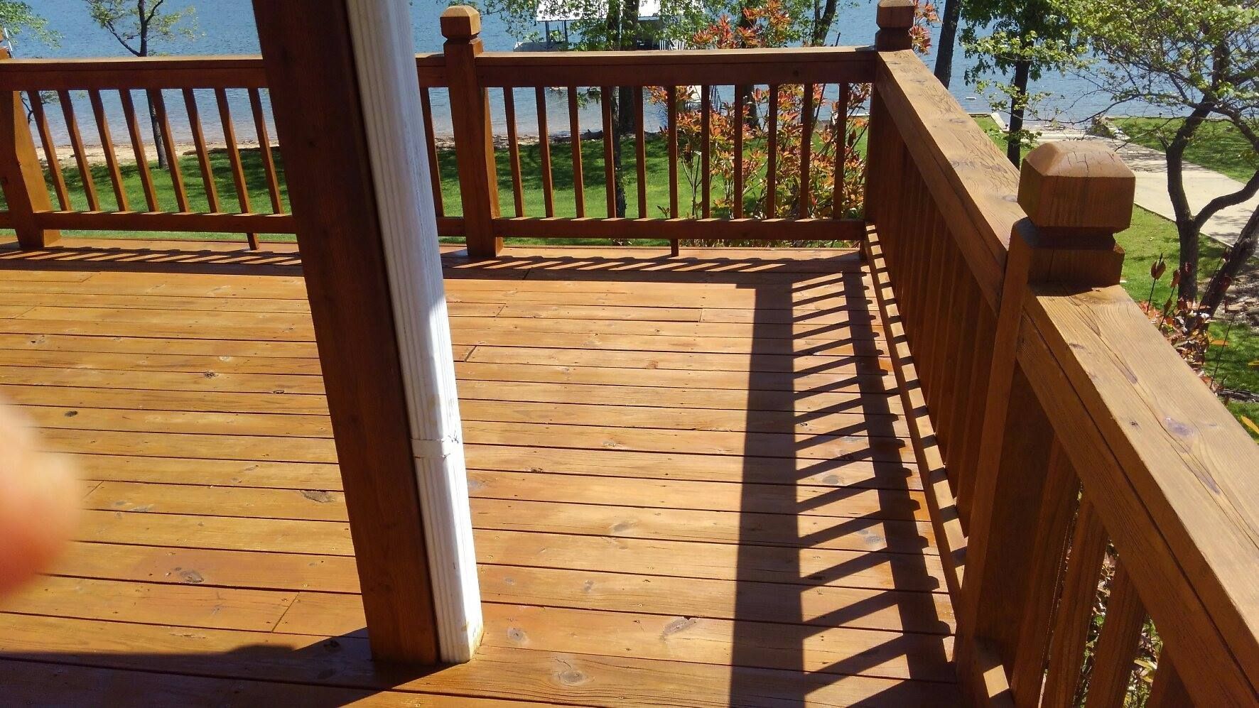 Wooden deck with railing overlooking a green landscape and water.