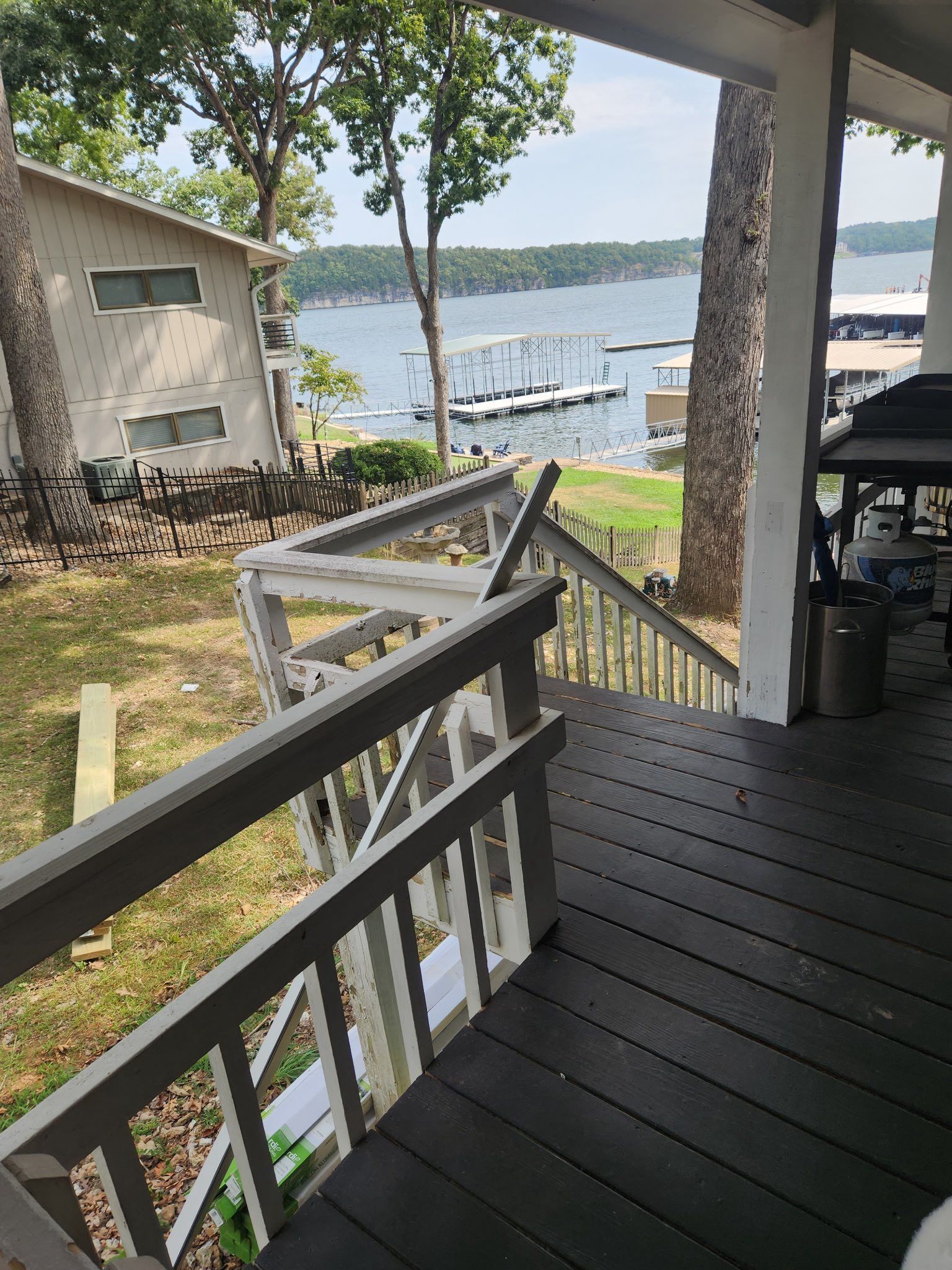 A porch with railing overlooks a lake, dock, and house.