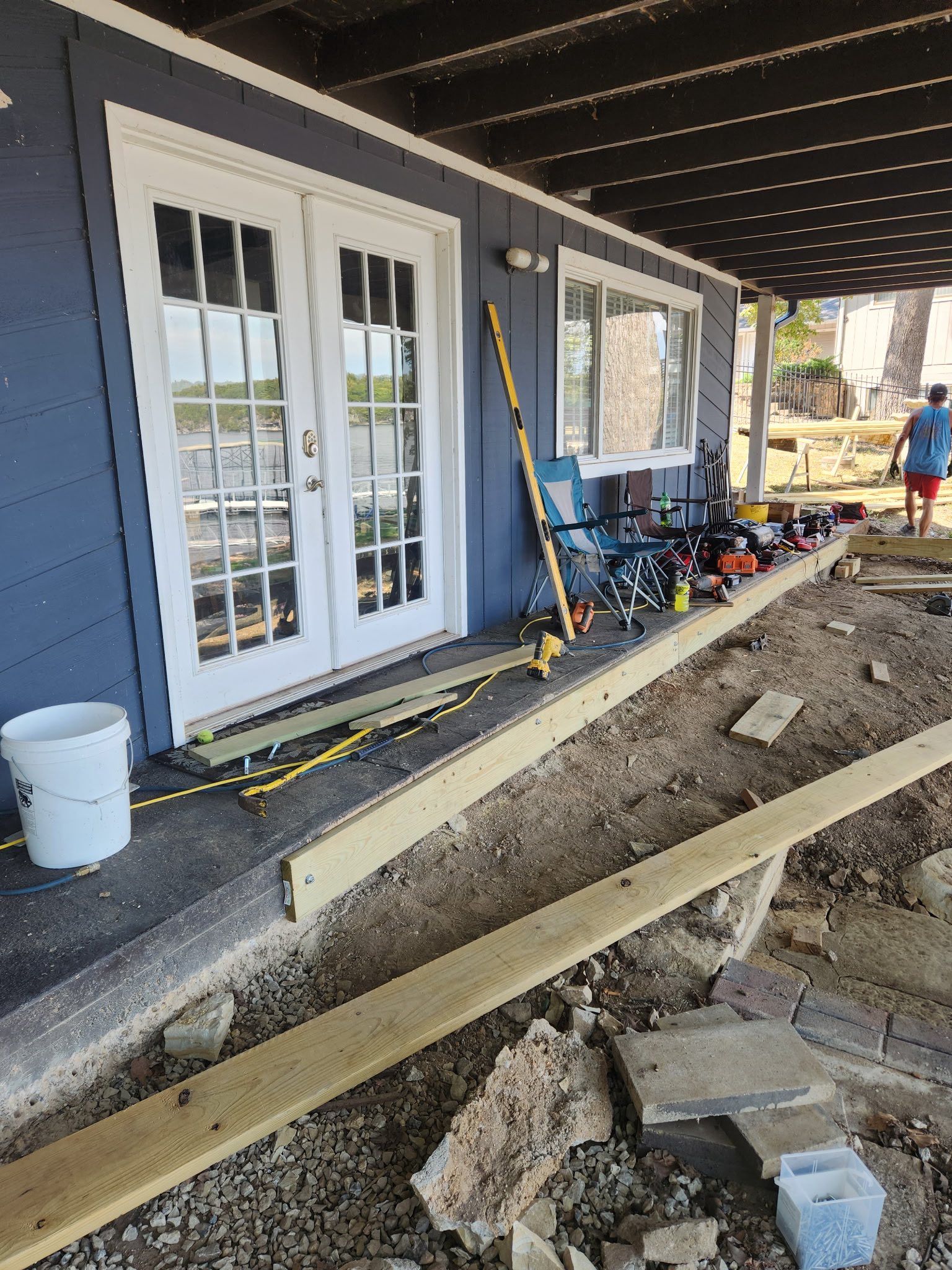 Construction site with wooden beams and tools against a blue building with double doors, under a covered area.