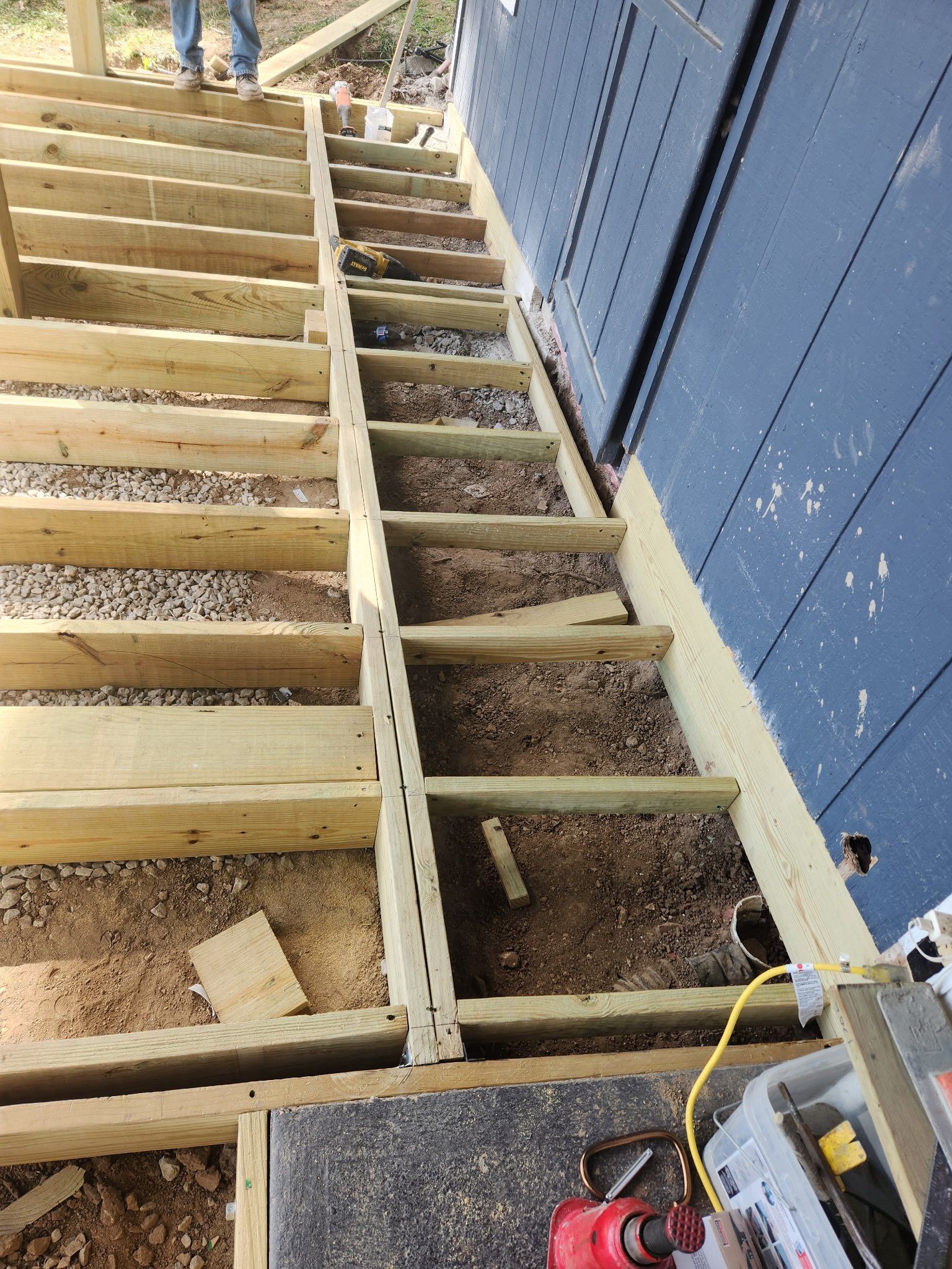 Wooden staircase under construction, next to a blue wall. Gravel between steps.
