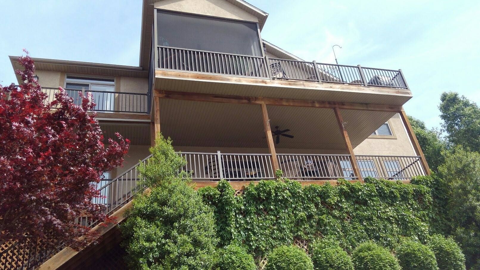 Multi-level home with decks and black awning against a blue sky, surrounded by green foliage.