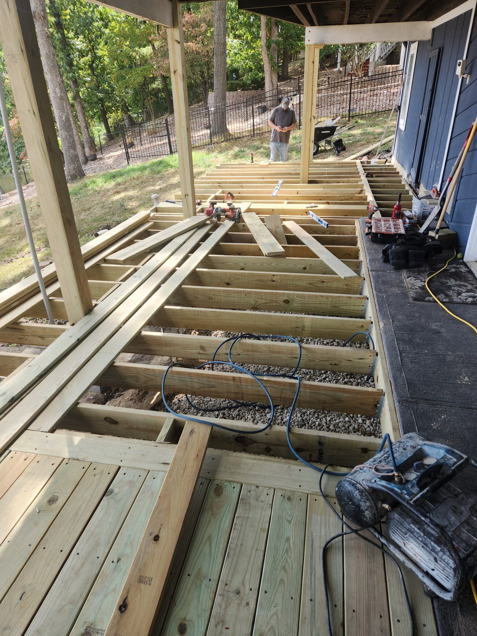 Deck construction with wooden planks, framing, tools, and a person working outdoors.