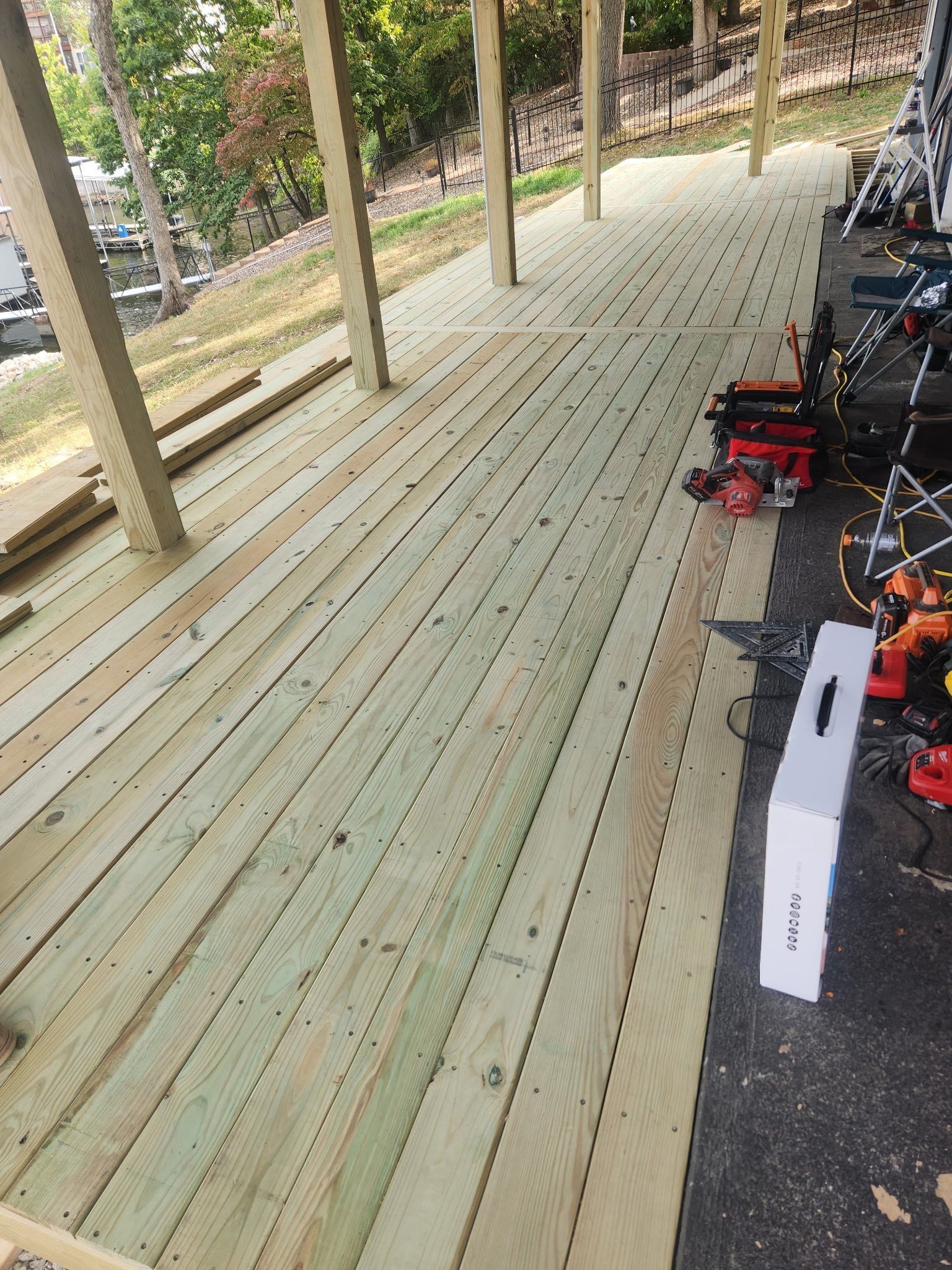 Newly constructed wooden deck with tools scattered on the surface. Green trees are in the background.