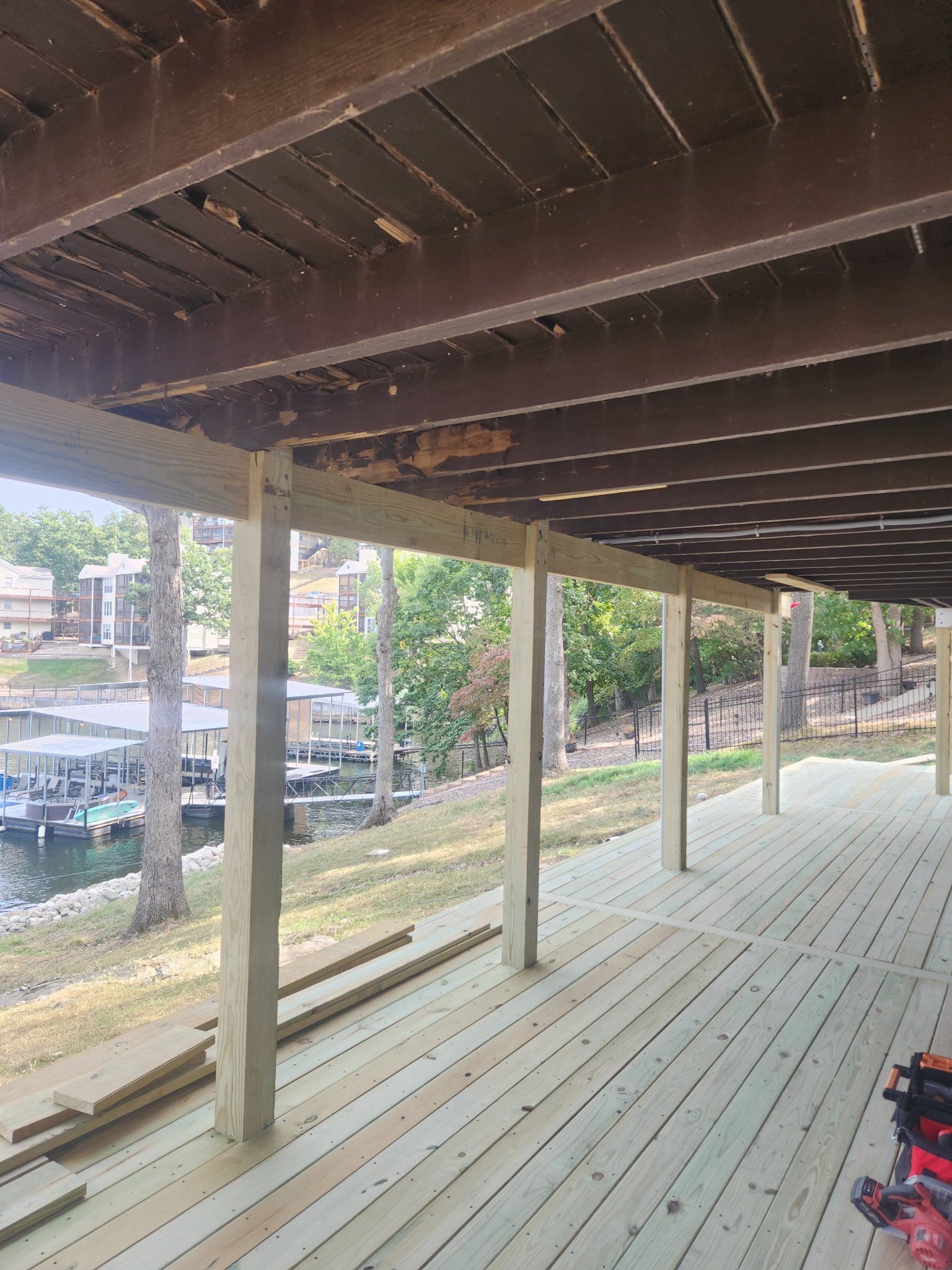 View of a partially constructed deck overlooking a lake, with new wooden posts and boards.