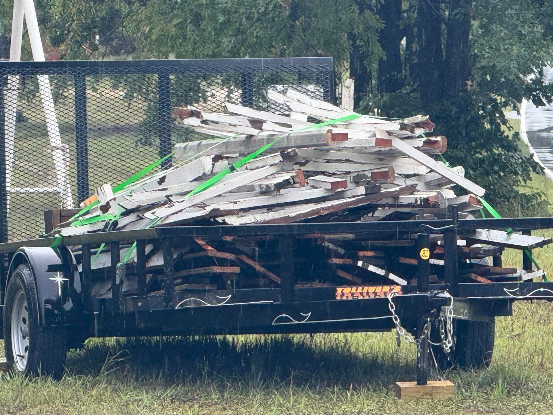 Trailer loaded with weathered metal sheets, secured with green straps.