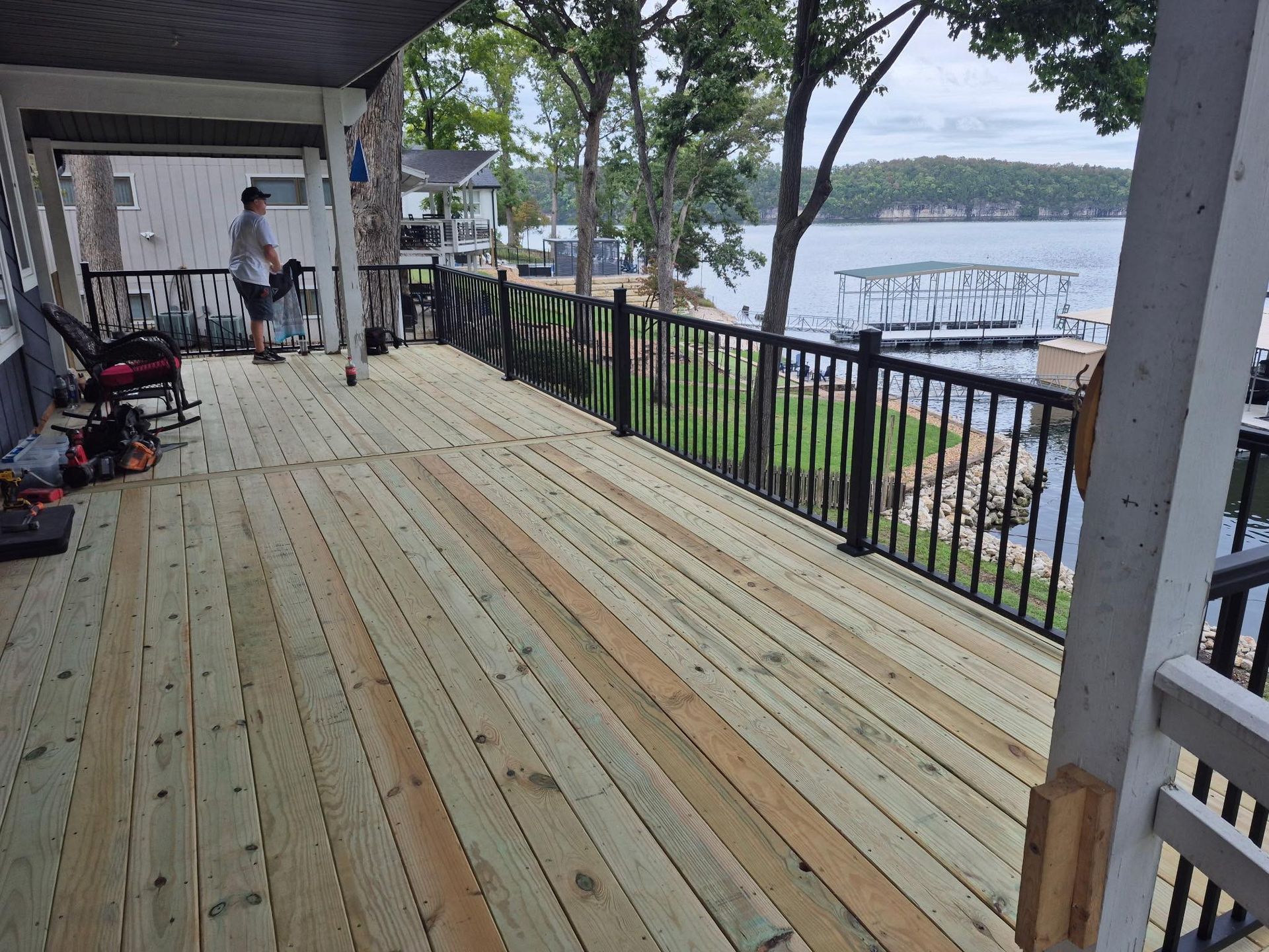 Wooden deck with black railing overlooking a lake. A person stands on the deck.