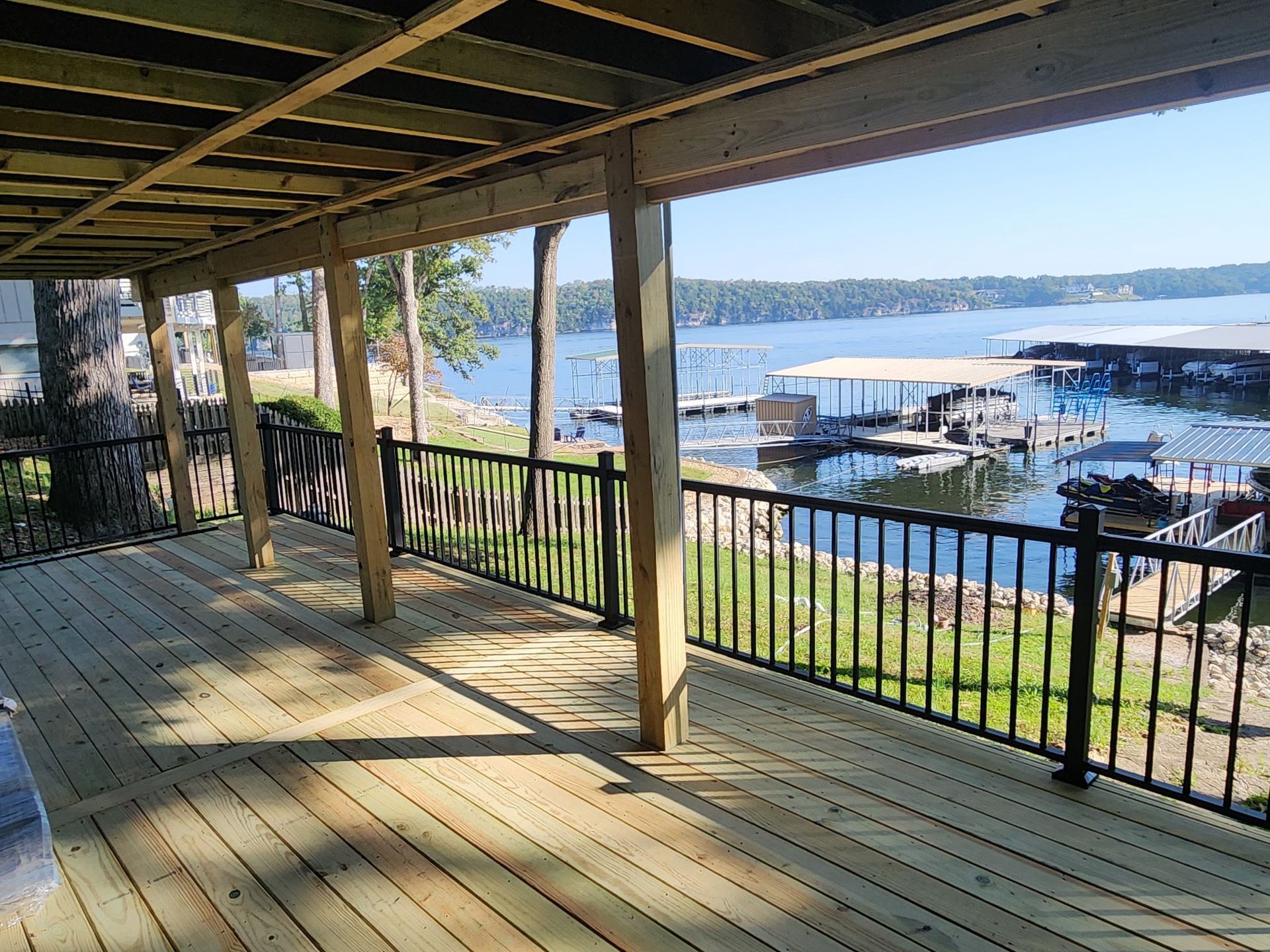 Wooden deck with black railing overlooking a lake with docks and a clear sky.