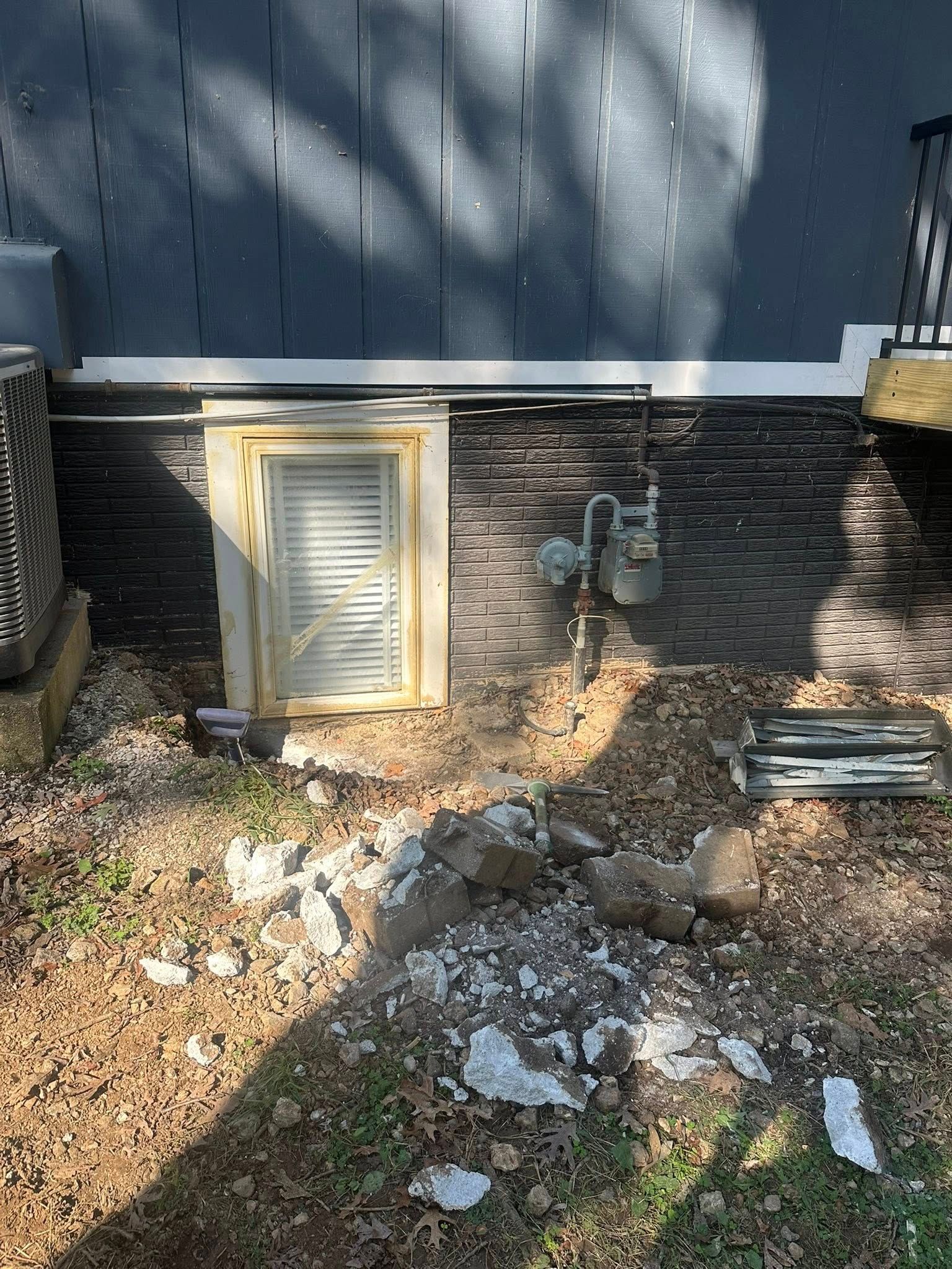 Exterior building with a window and gas meter. Ground is uneven with rocks and dirt.