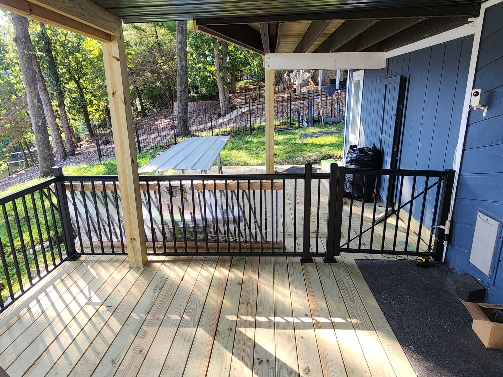 Covered porch deck with black railing, wood posts, and steps overlooking a grassy yard